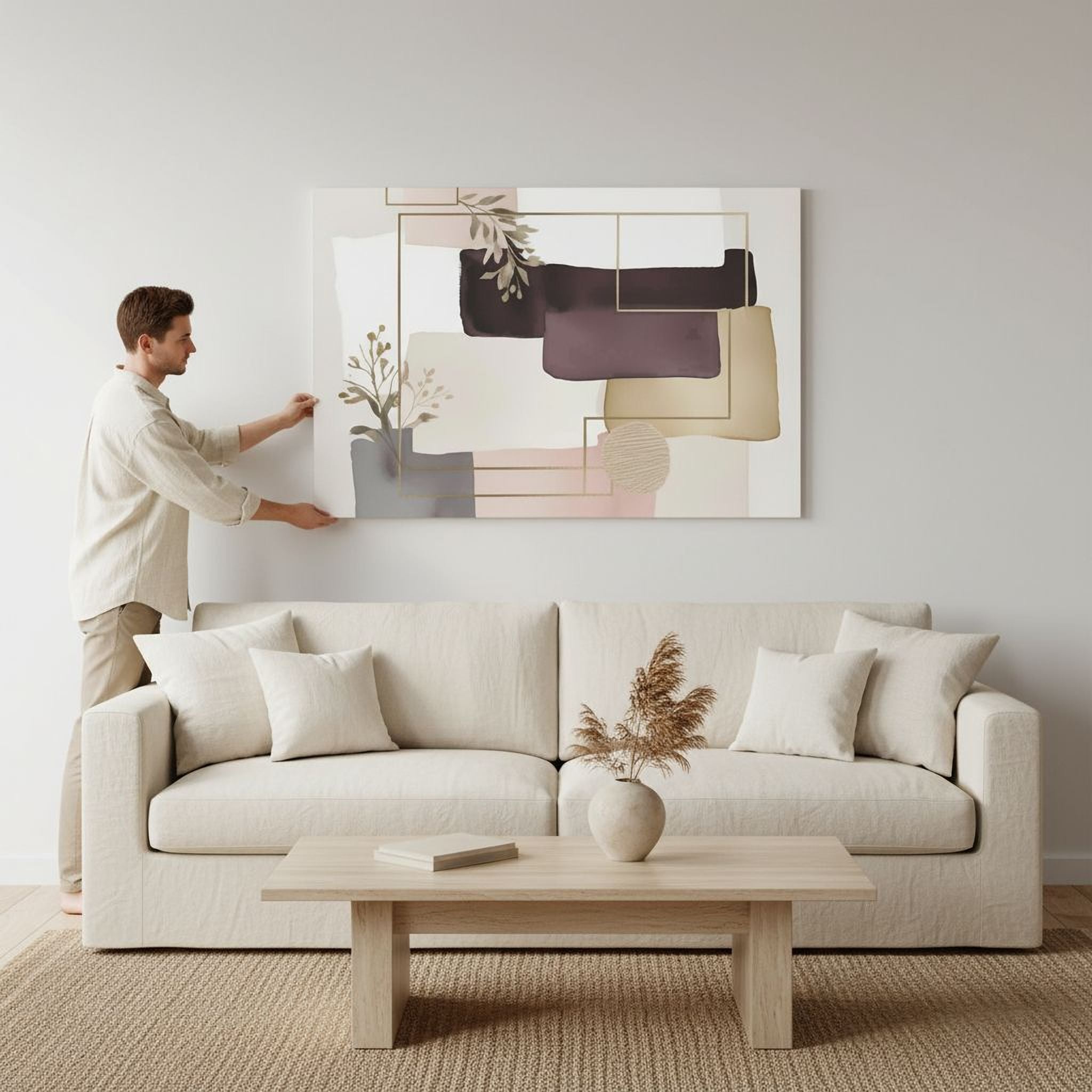 A man is hanging a large abstract painting on a wall in a living room.