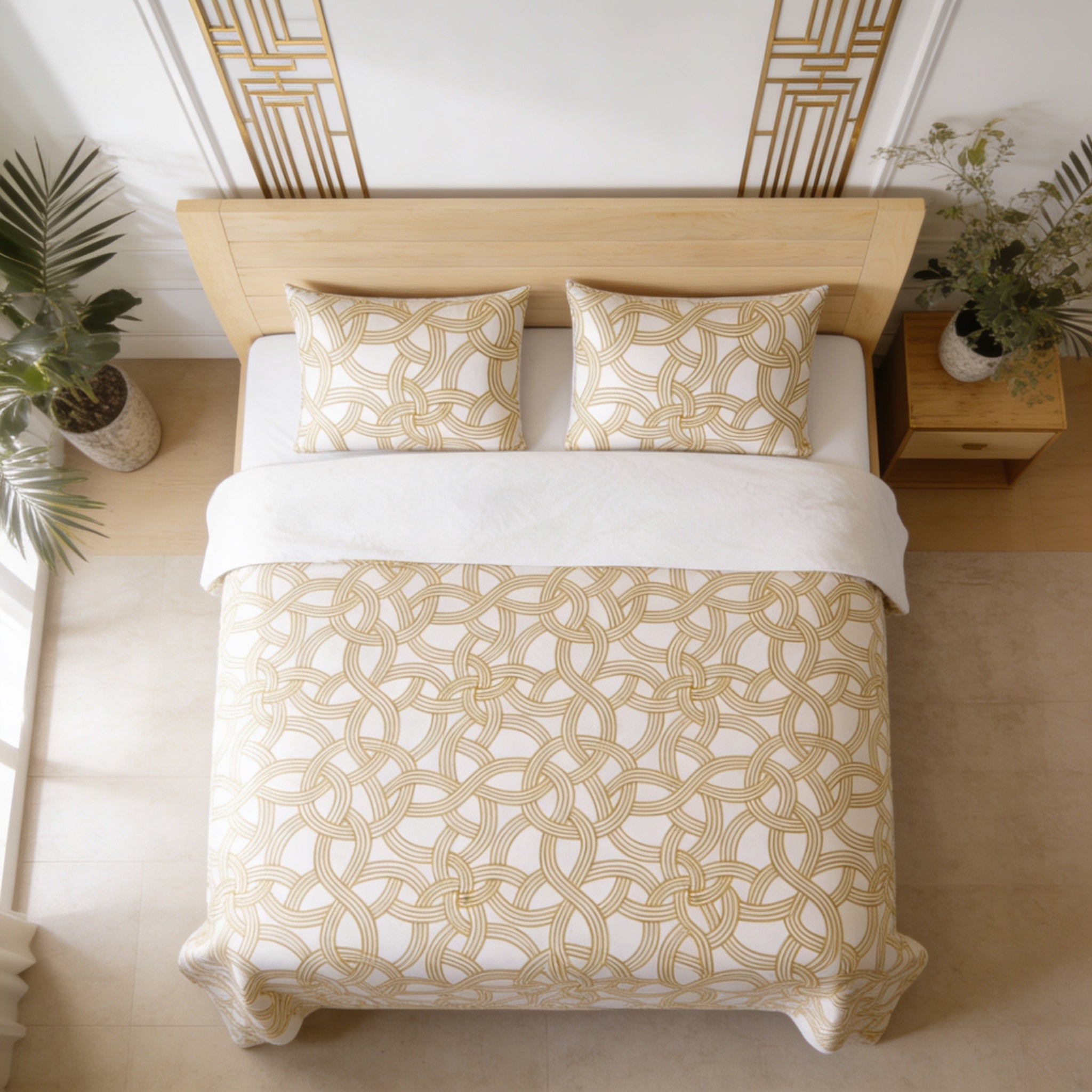 a neatly made bed with a white and gold patterned comforter and pillows, along with a wooden headboard. The bed is positioned against a wall with a decorative gold frame. There are also two potted plants in the room, one on the left side and the other on the right side.