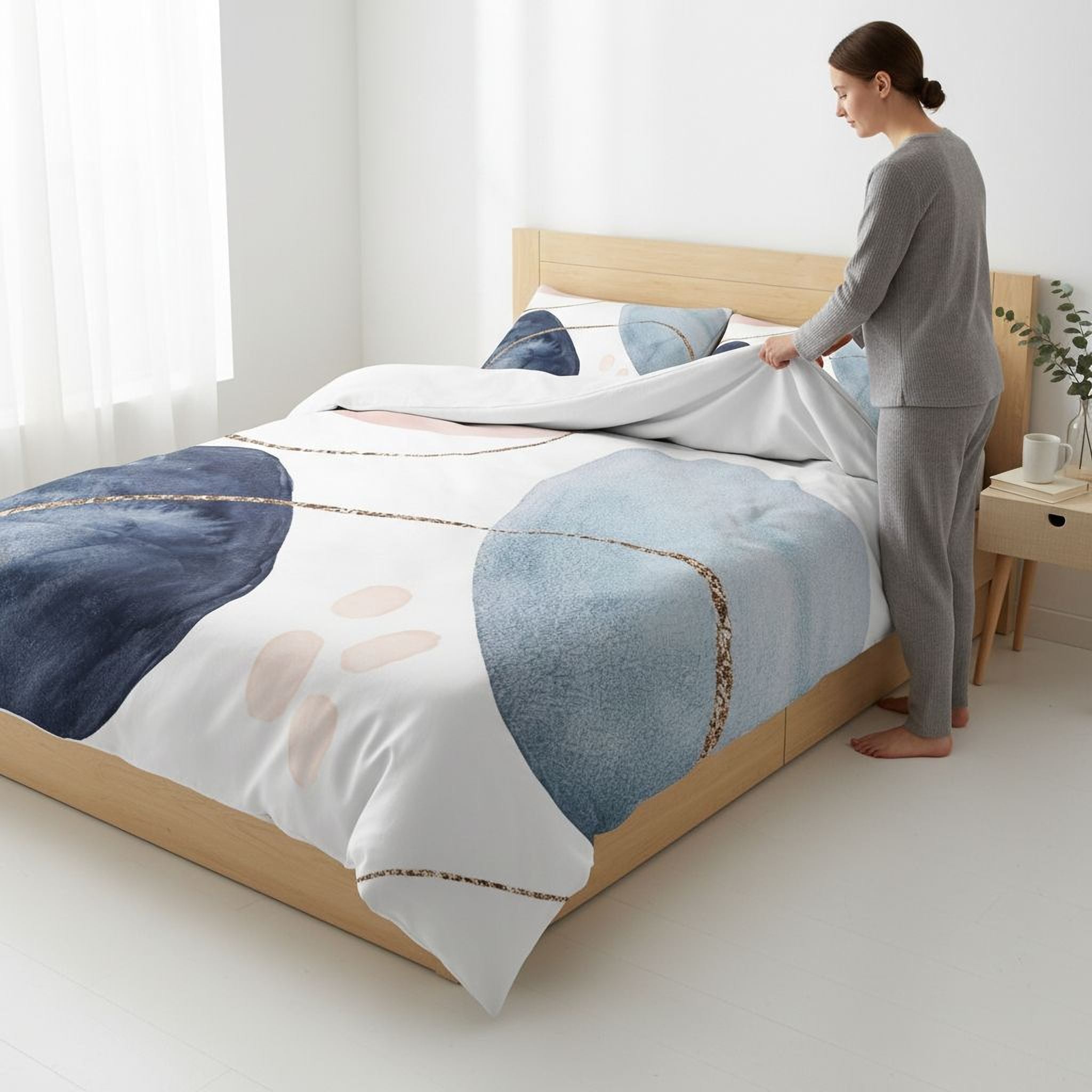 A woman is making the bed in a bedroom with a modern, abstract-patterned comforter and pillows.