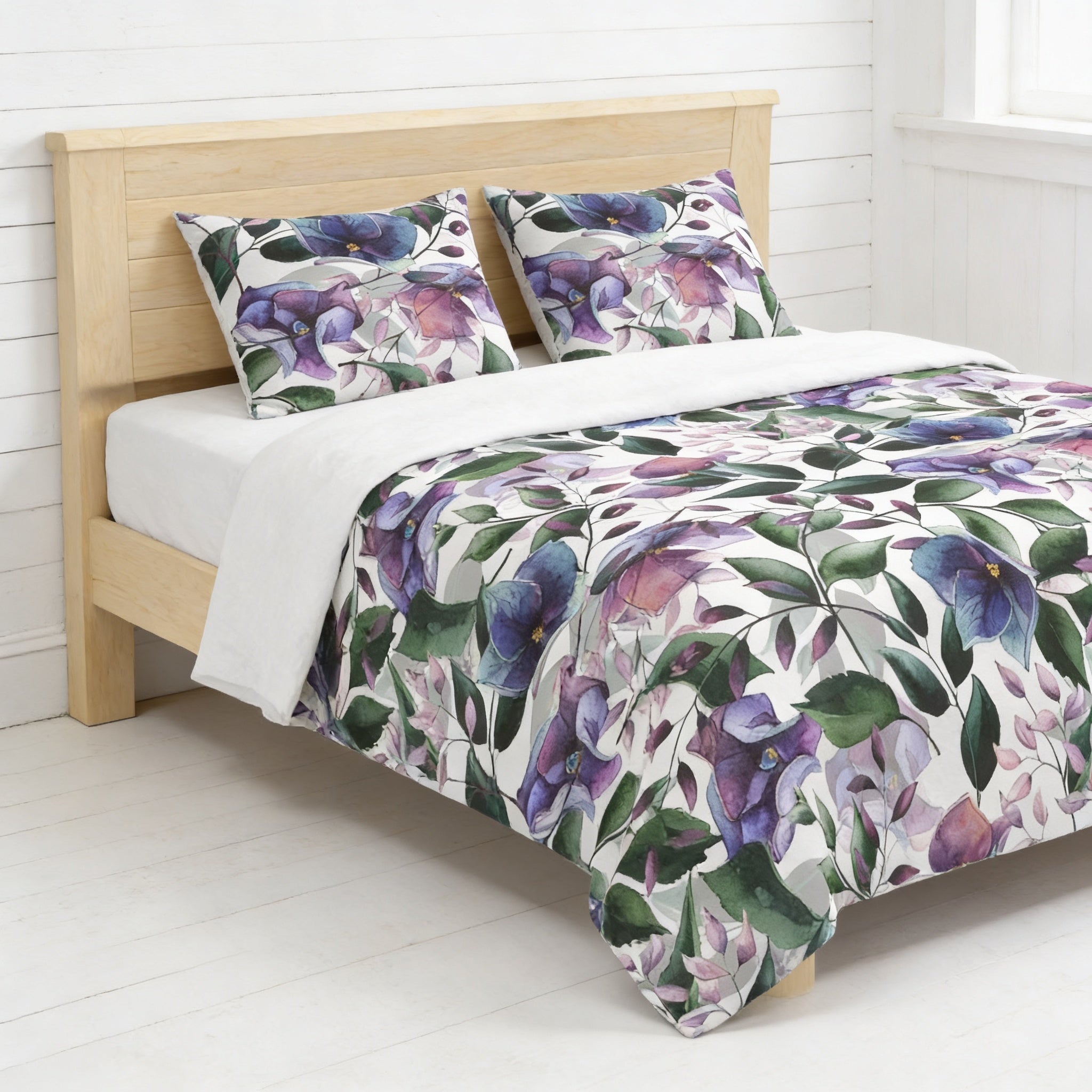 a bed with a floral print comforter and pillows, set against a white wall and wooden headboard.