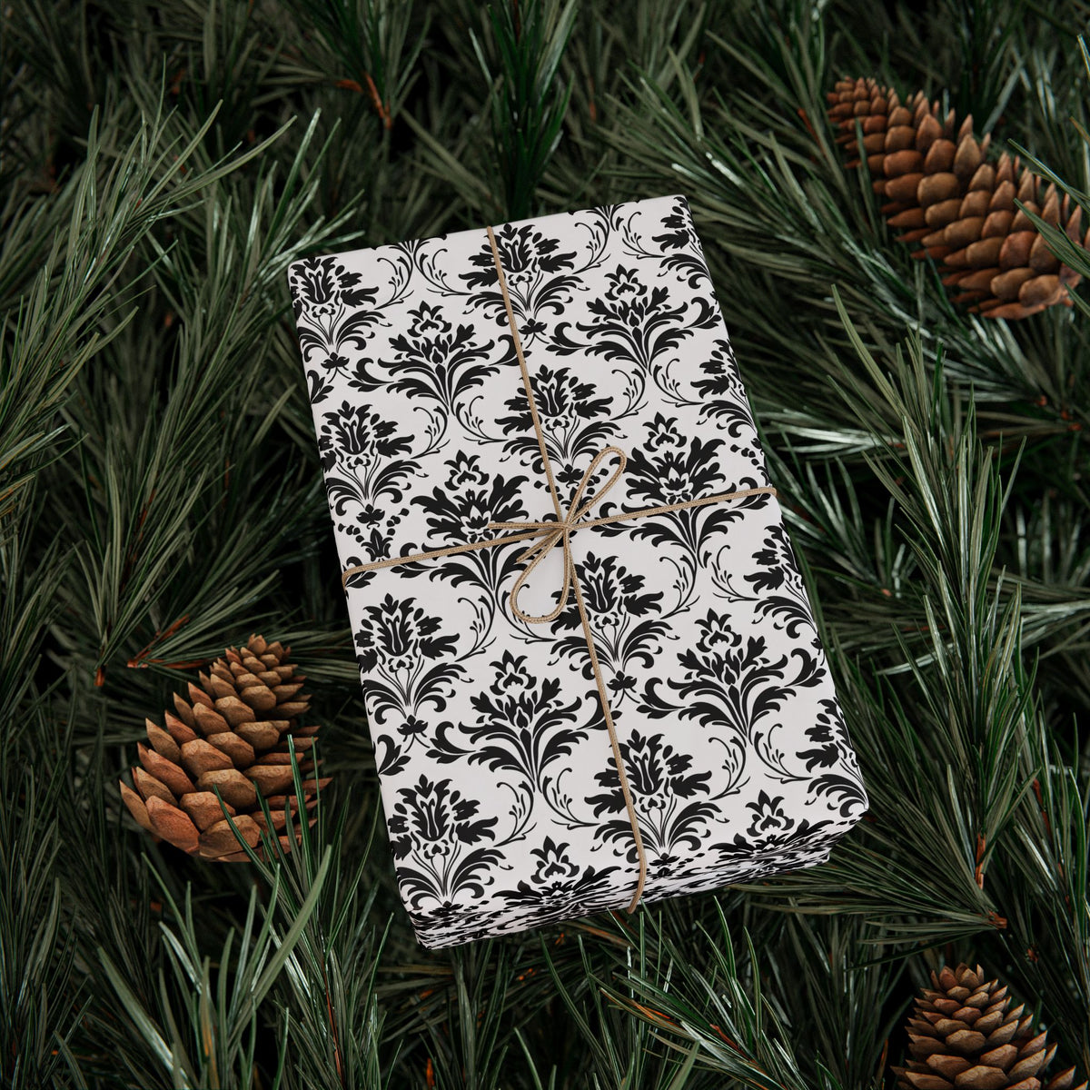 Gift wrapped in classic black and white damask wrapping paper on pine branches with pinecones