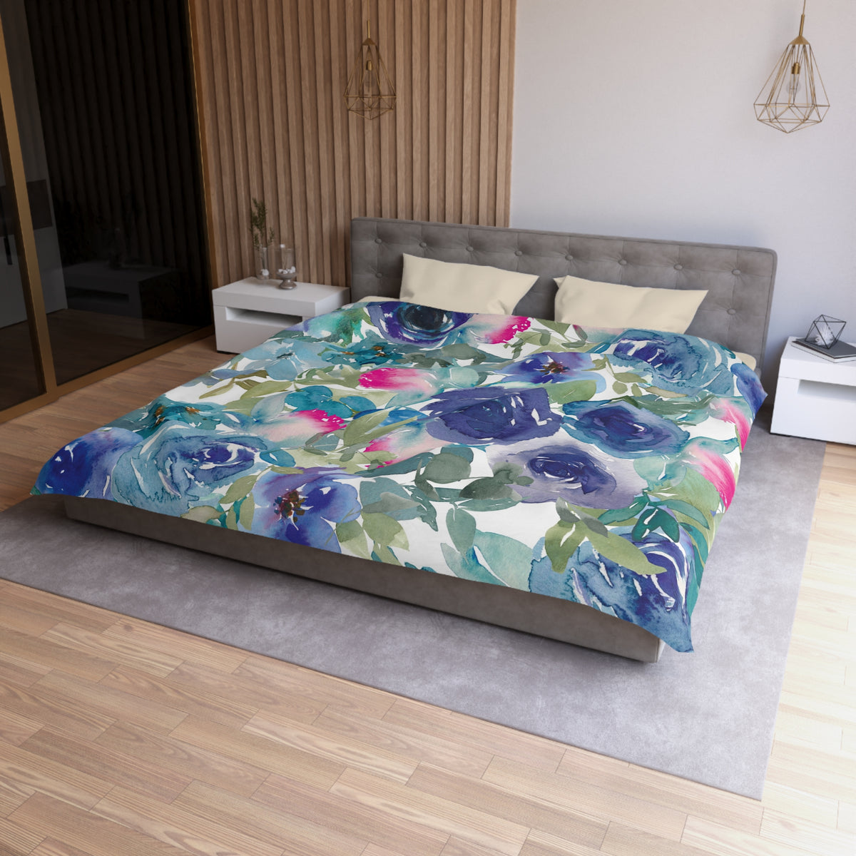 a bedroom with a large bed covered in a colorful floral comforter. The bed is positioned against a wall with a wooden panel. The room has a modern and minimalist design, with a gray headboard and white nightstands.