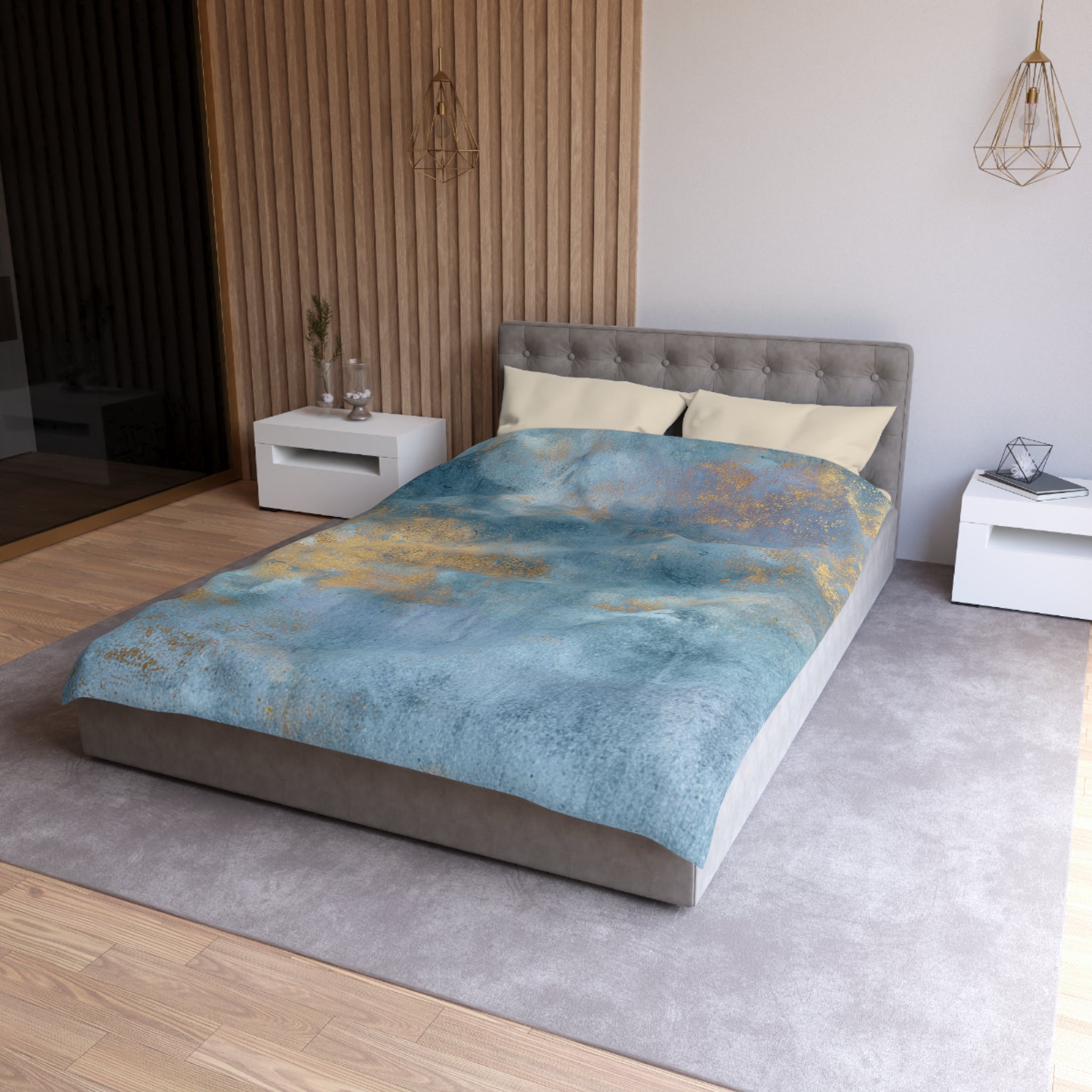 a modern bedroom with a large bed, a gray headboard, and a blue and gold patterned comforter. The room has a neutral color scheme with white walls and a wooden floor. There are two nightstands on either side of the bed, and a pendant light hangs above the bed.