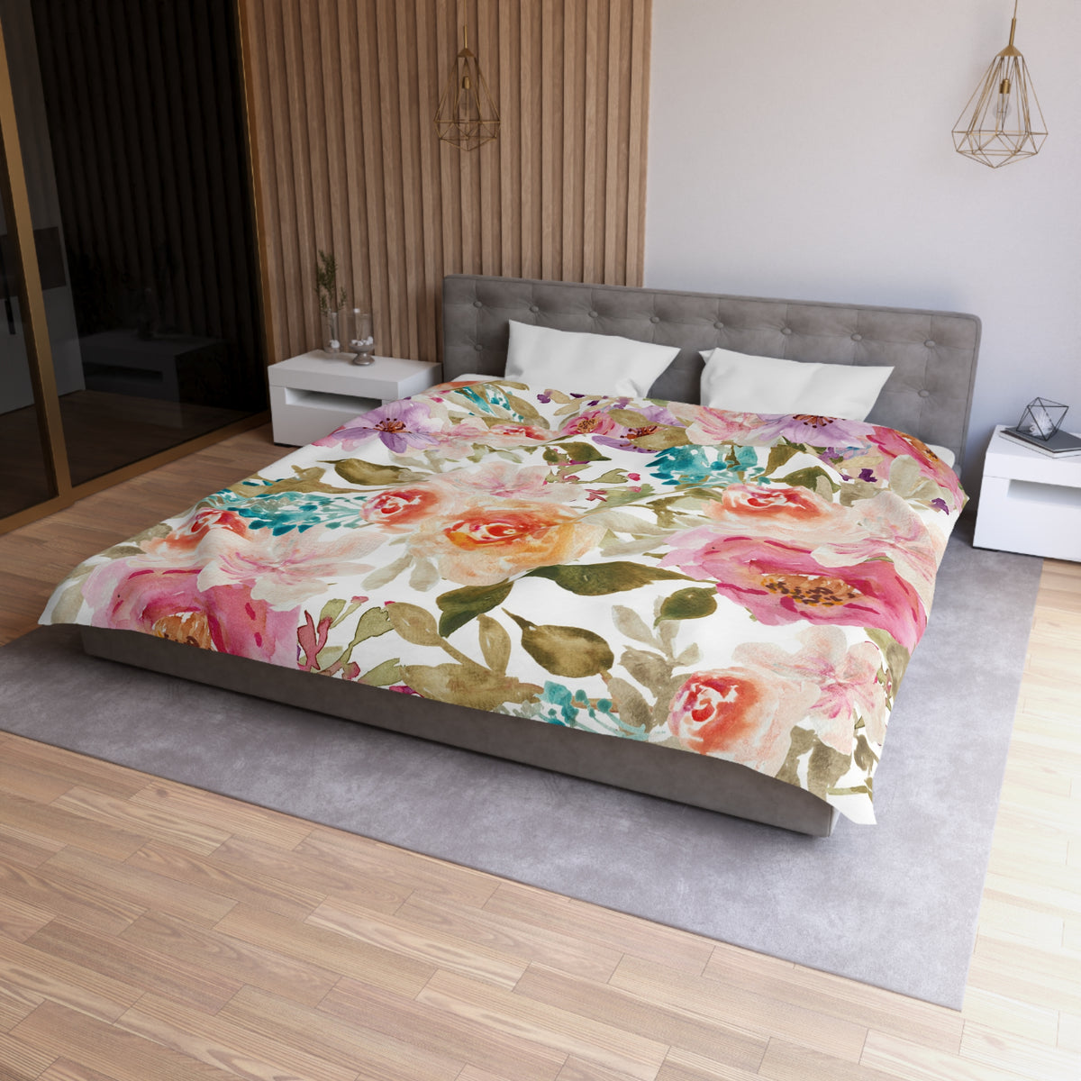 a bedroom with a large bed covered in a floral print comforter. The bed is positioned against a wall with a wooden panel. The room has a gray headboard and a white nightstand on each side of the bed. There is also a pendant light hanging above the bed.