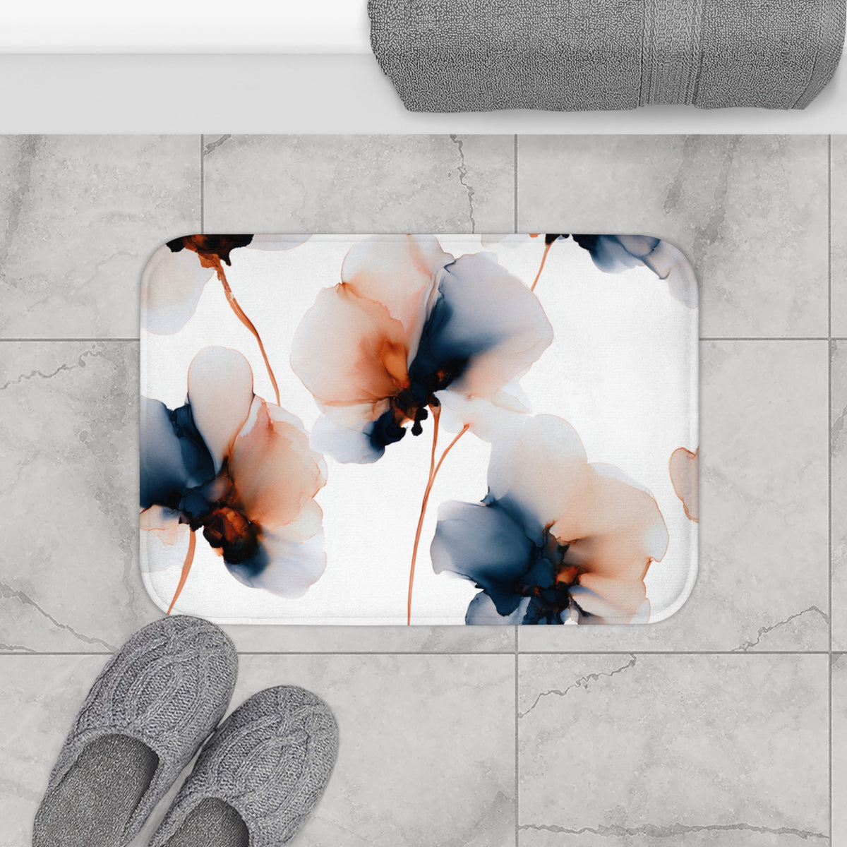 a bathroom scene with a floral patterned bath mat, gray slippers, and a rolled-up towel on the counter.