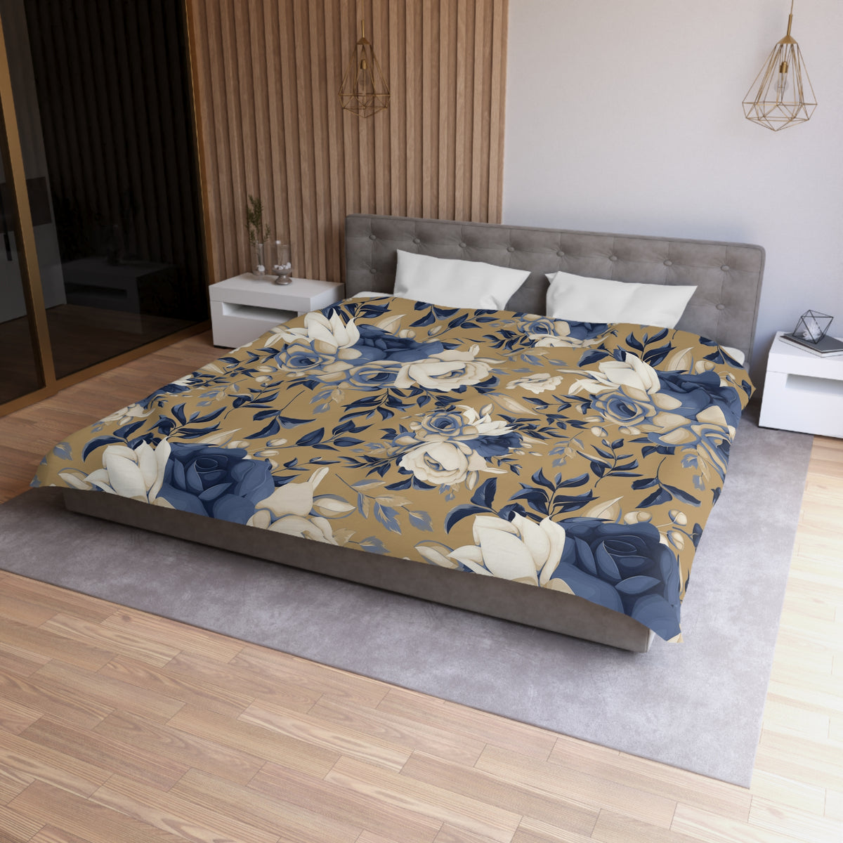 a bedroom with a large bed covered in a floral print comforter. The bed is positioned against a wall with a wooden panel. The room has a wooden floor and a white nightstand on the left side of the bed. There is also a pendant light hanging above the bed.