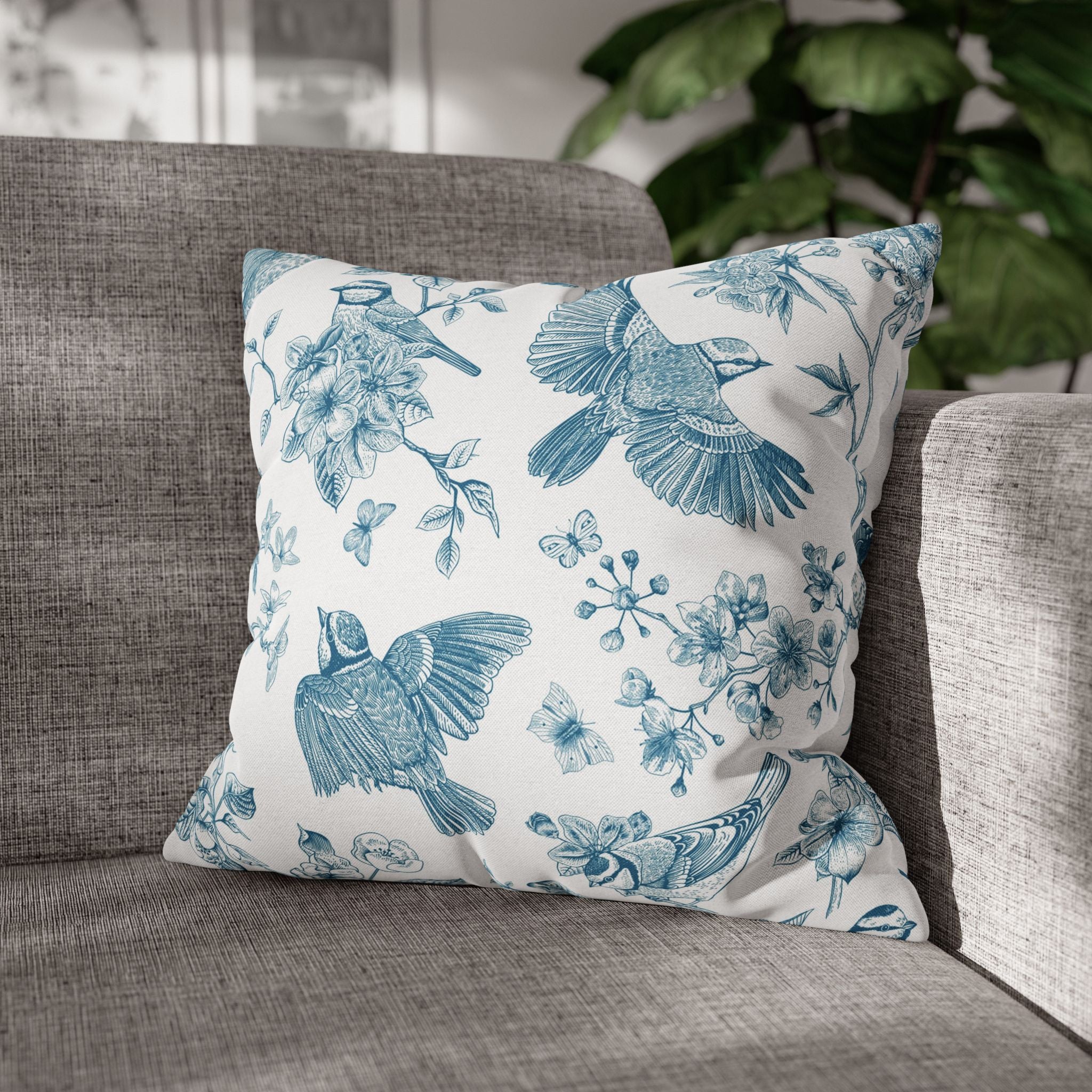 A gray sofa with a white throw pillow featuring a blue floral and bird pattern.