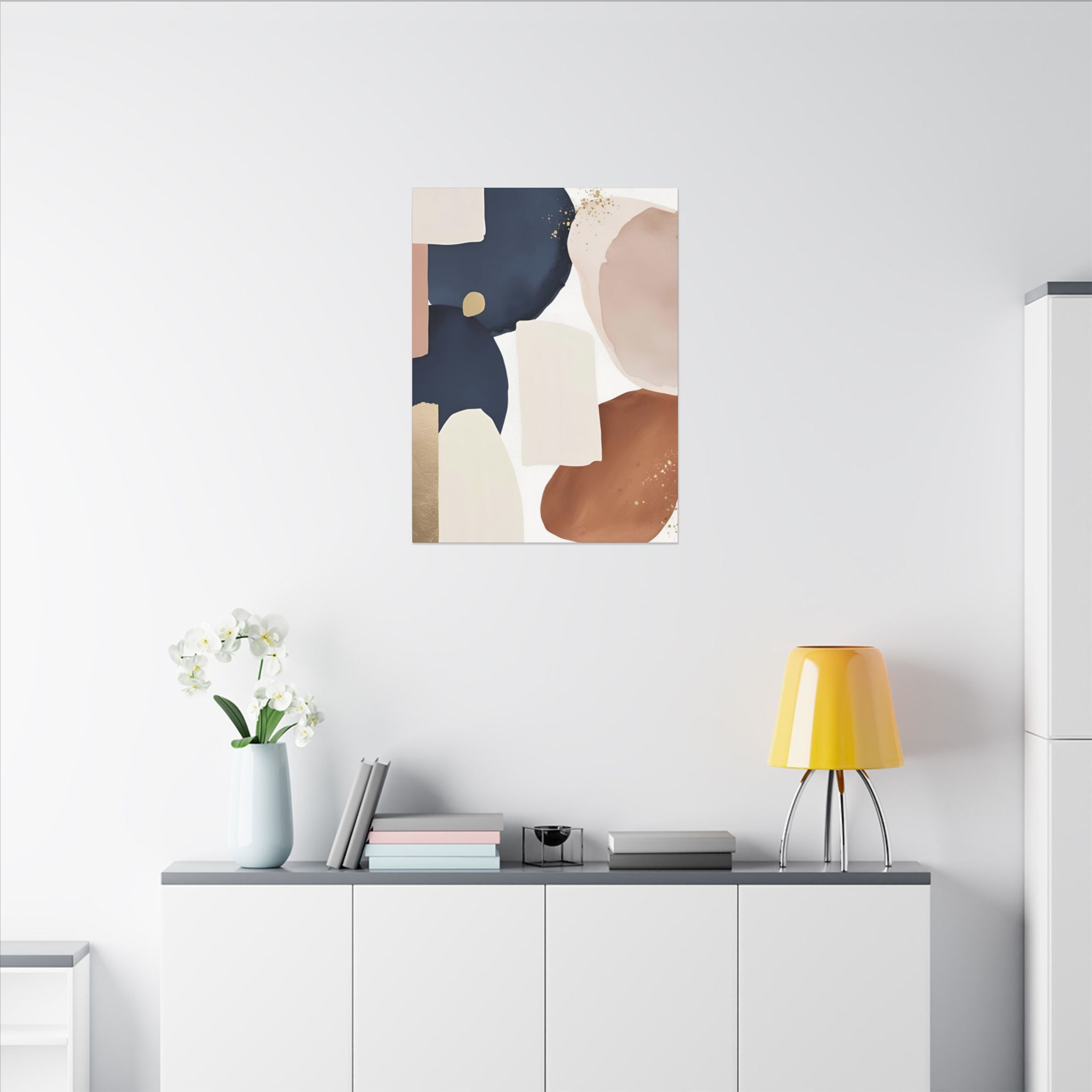 a minimalist living space with a white wall, a white cabinet, a yellow lamp, a vase with white flowers, and a framed abstract art piece hanging above the cabinet.