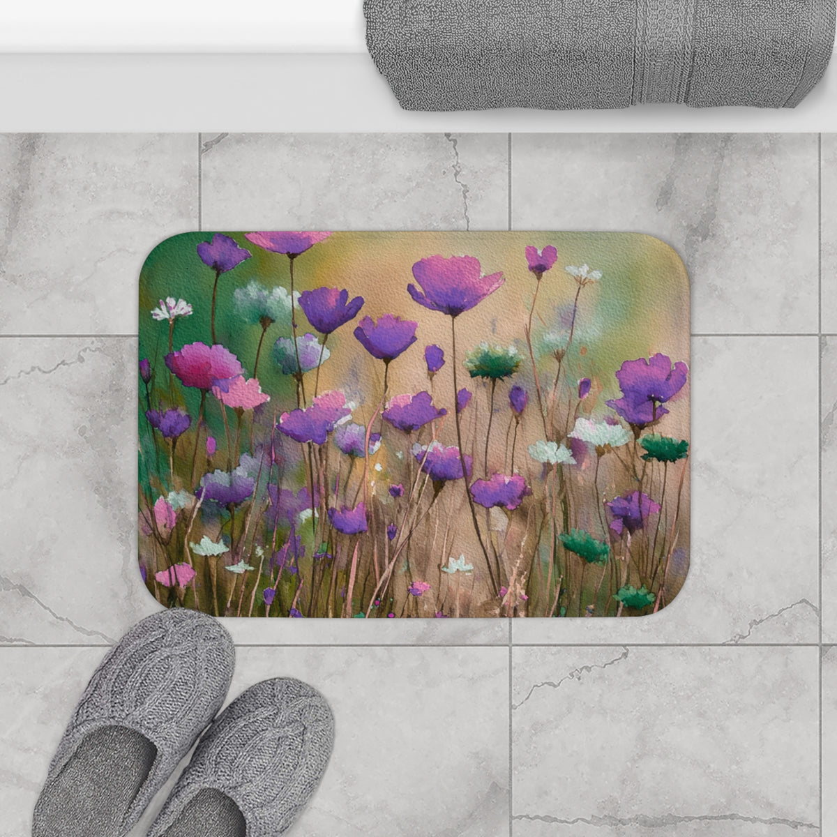 a bathroom mat with a floral design, including purple and white flowers, placed on a tiled floor. There are also gray slippers and a rolled-up towel visible in the scene.