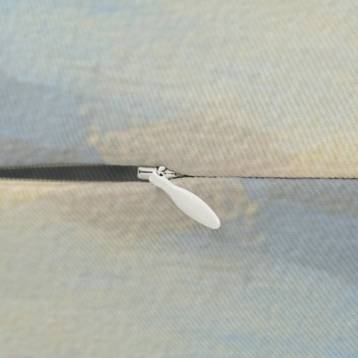 A close-up view of a zipper on a fabric, with a white plastic zipper pull visible.