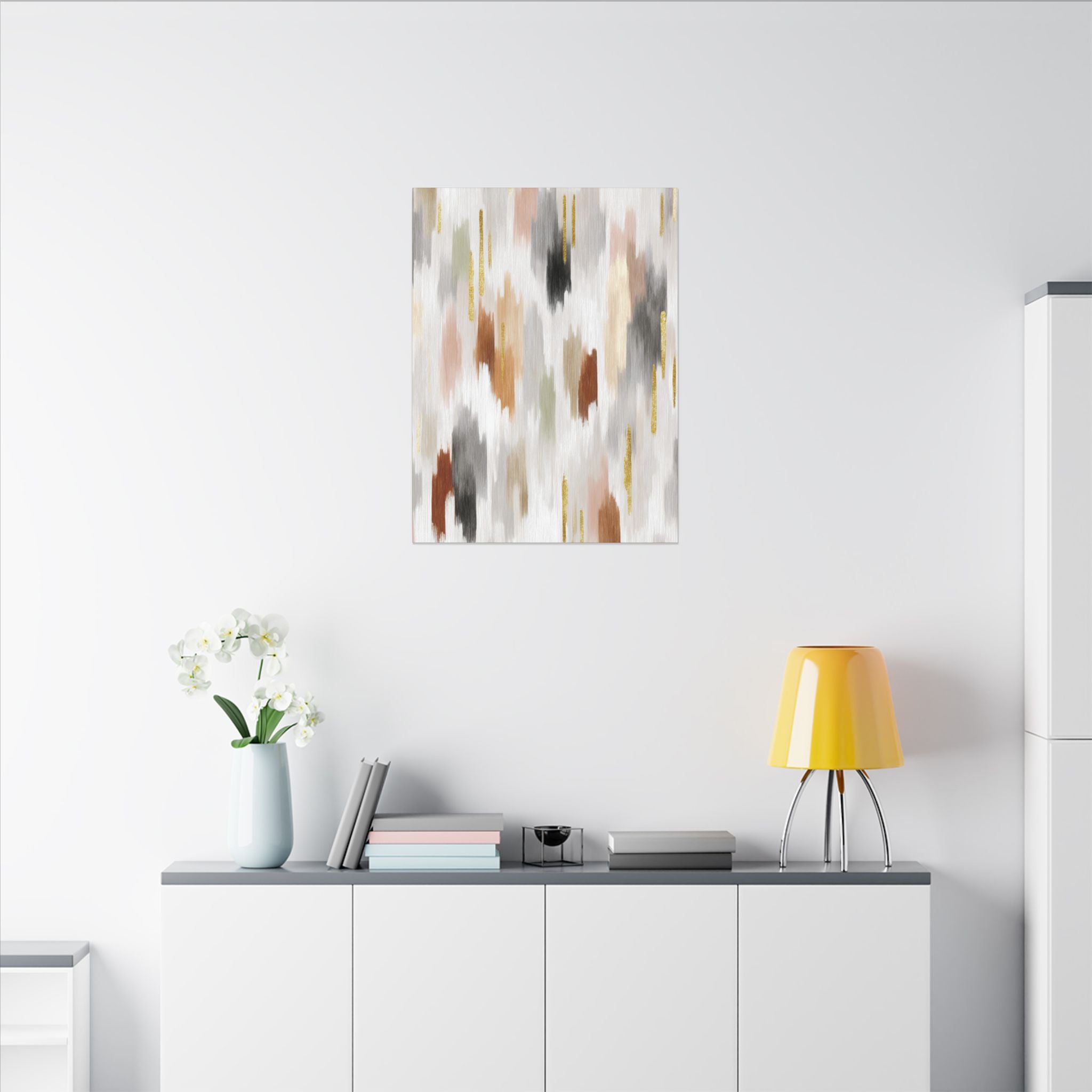 a minimalist living space with a white wall, a white cabinet, a yellow lamp, a vase with white flowers, and a framed abstract painting above the cabinet.