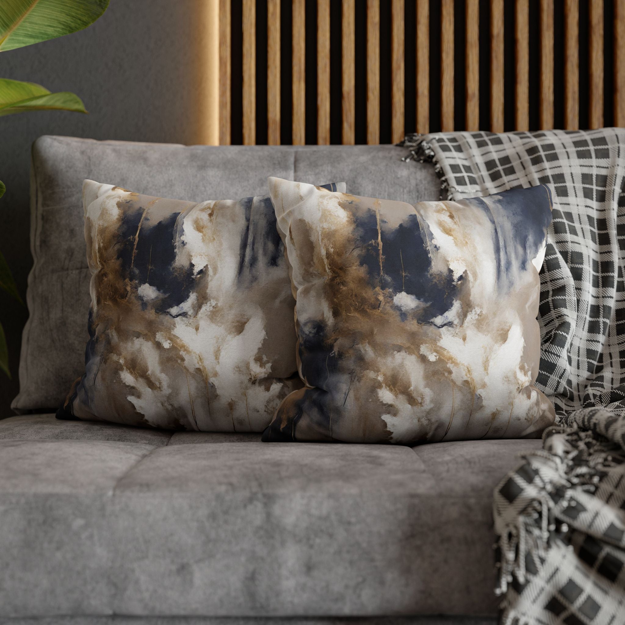 a gray couch with two decorative pillows on it, one with a blue and white abstract pattern and the other with a black and white checkered pattern. The pillows are placed on a gray couch, and there is a wooden wall and a plant in the background.