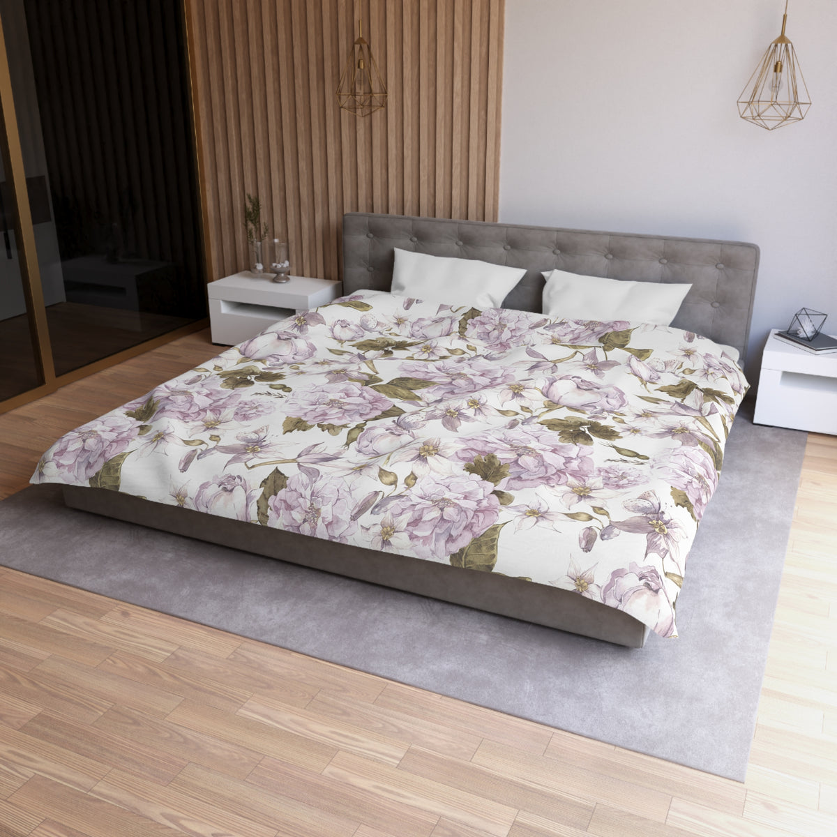a modern bedroom with a large bed covered in a floral print comforter. The bed is positioned against a wall with a wooden panel. The room has a minimalist design, with a gray headboard and white nightstands. There is a pendant light hanging above the bed, and a vase on one of the nightstands. The overall color scheme of the room is neutral, with the floral print and gray tones creating a harmonious and serene atmosphere.