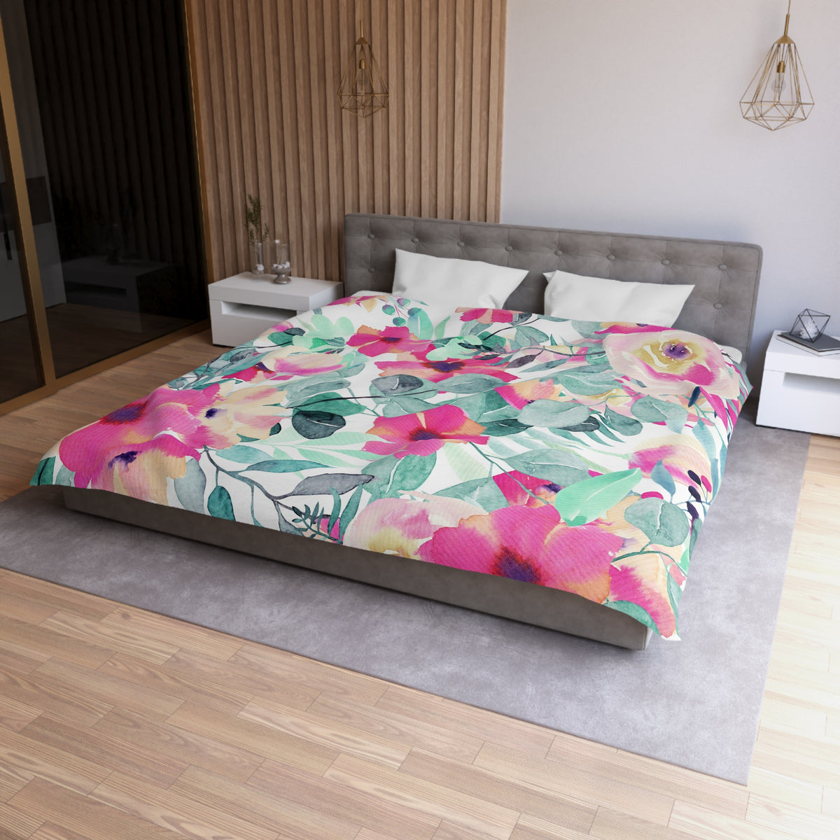 a modern bedroom with a large bed covered in a colorful floral comforter. The bed is positioned against a wall with a wooden panel. The room has a gray headboard and a white nightstand on each side of the bed. There is also a pendant light hanging above the bed.