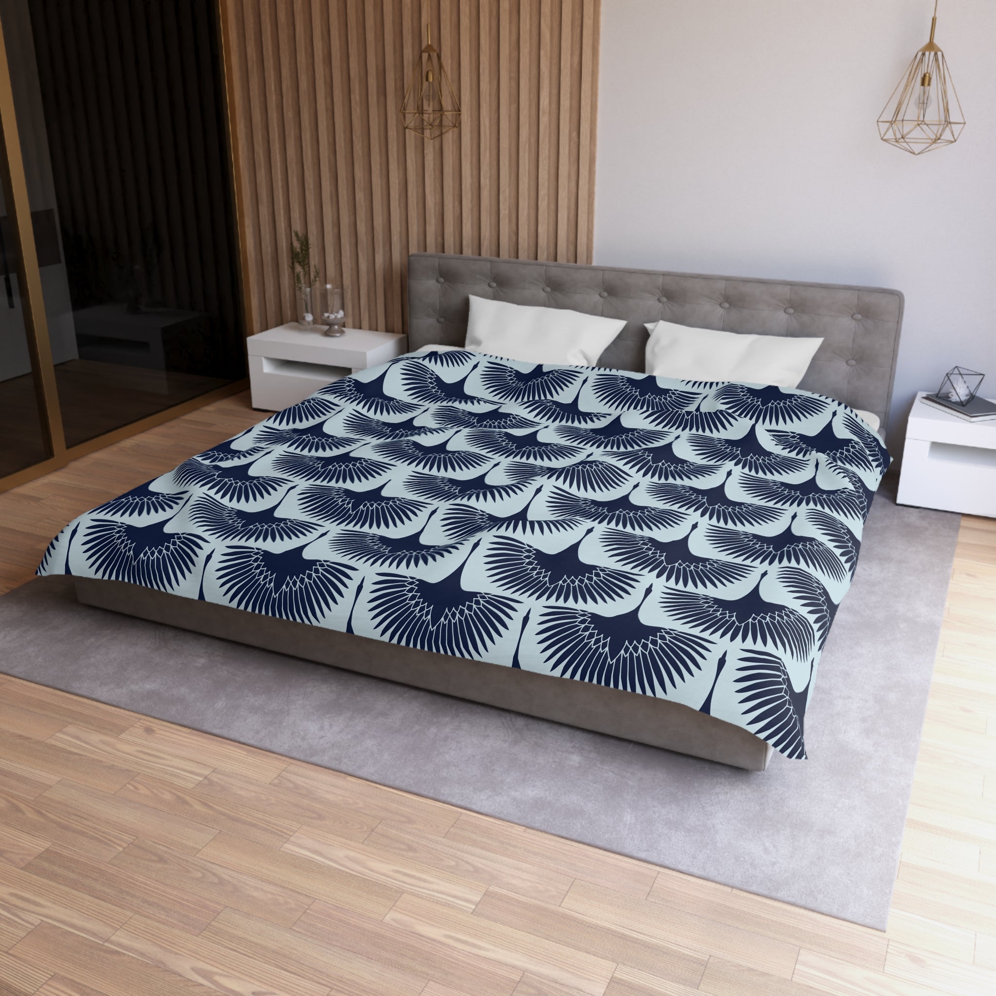 a modern bedroom with a large bed featuring a blue and white patterned comforter. The bed is positioned against a wall with a wooden panel. The room also includes a nightstand and a pendant light fixture.