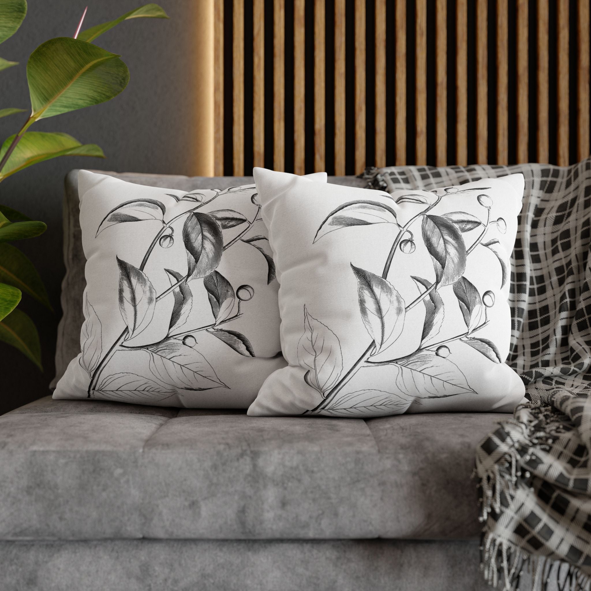 a gray couch with two white throw pillows with black leaf designs, placed on top of it. The pillows are positioned in a way that they appear to be resting on the couch.