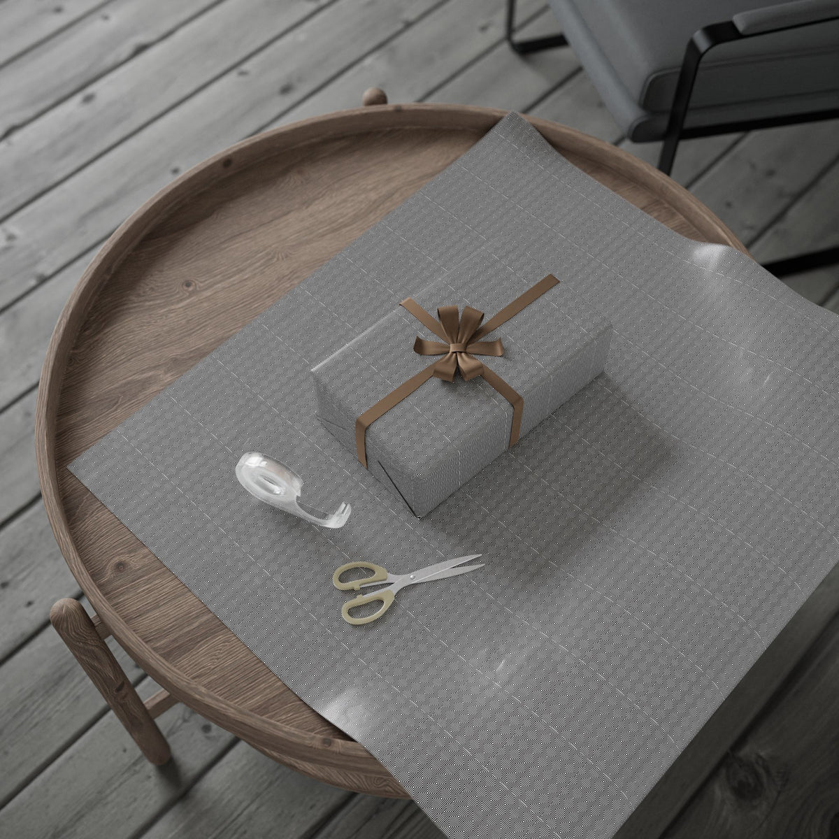 A wooden table with a gray tablecloth, a gift box with a brown bow, a pair of scissors, and a roll of tape on it.