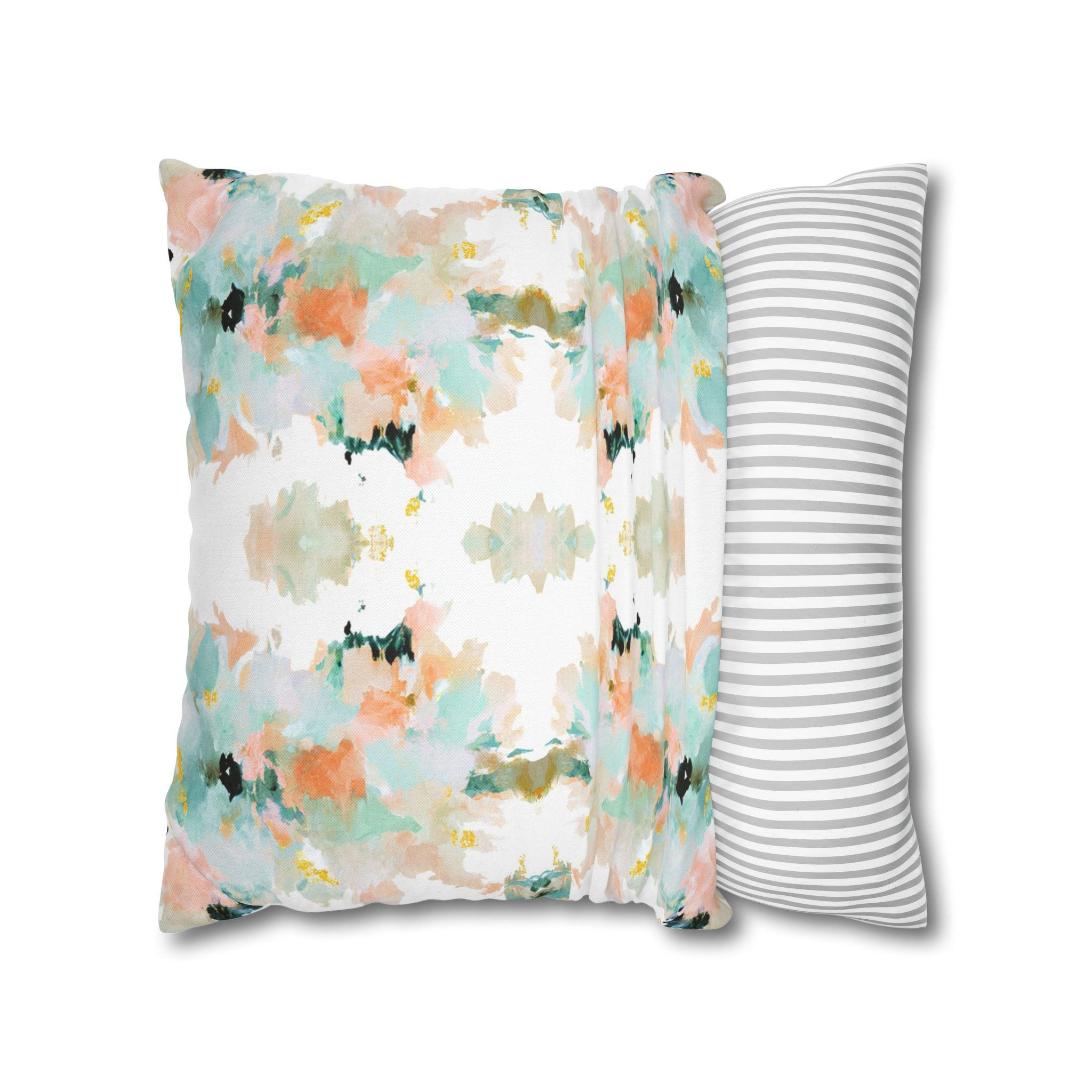 a square throw pillow with a vibrant abstract floral pattern in shades of green, orange, and white. The pillow is placed next to a striped pillow, creating a visually appealing contrast between the two.