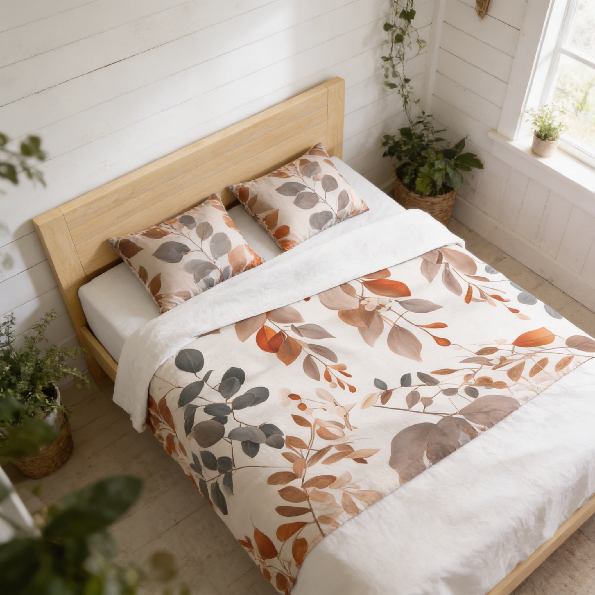 a cozy bedroom with a bed adorned with a leafy, autumn-themed bedspread and pillows. The room is decorated with potted plants, adding a touch of greenery to the space. The overall atmosphere is warm and inviting, with the natural elements complementing the wooden furniture and white walls.
