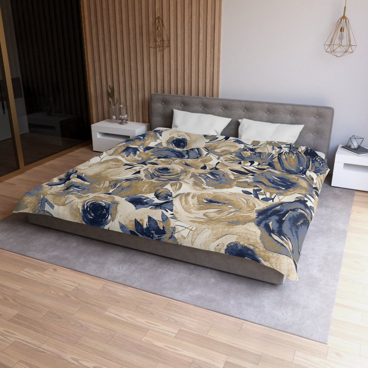a modern bedroom with a large bed covered in a floral print comforter. The bed is positioned against a wall with a wooden panel. The room has a wooden floor and a white nightstand on the left side of the bed. There is also a pendant light hanging above the bed.