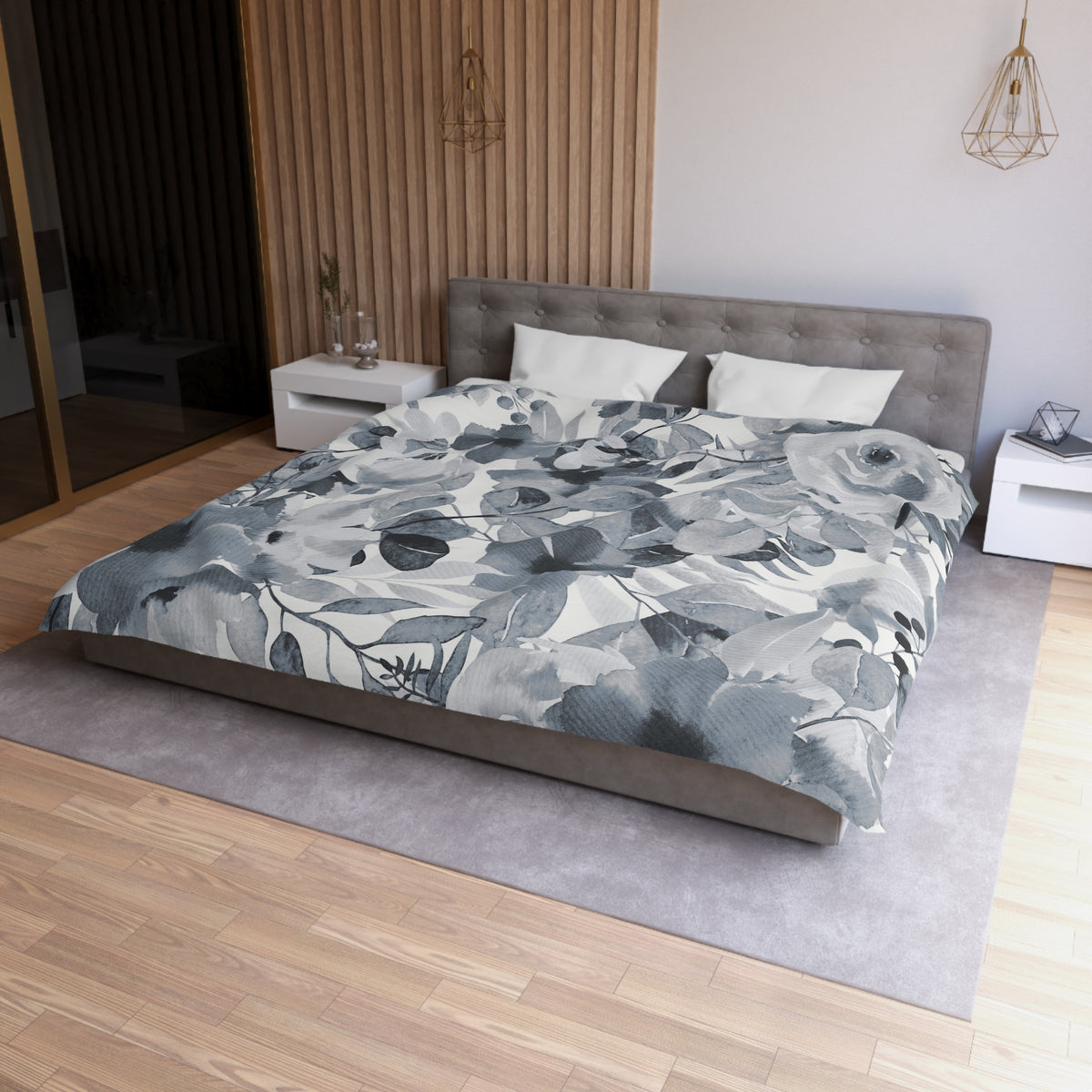 a modern bedroom with a large bed covered in a gray and white floral comforter. The bed is positioned against a wall with a wooden panel. The room also features a nightstand, a pendant light, and a rug on the floor.