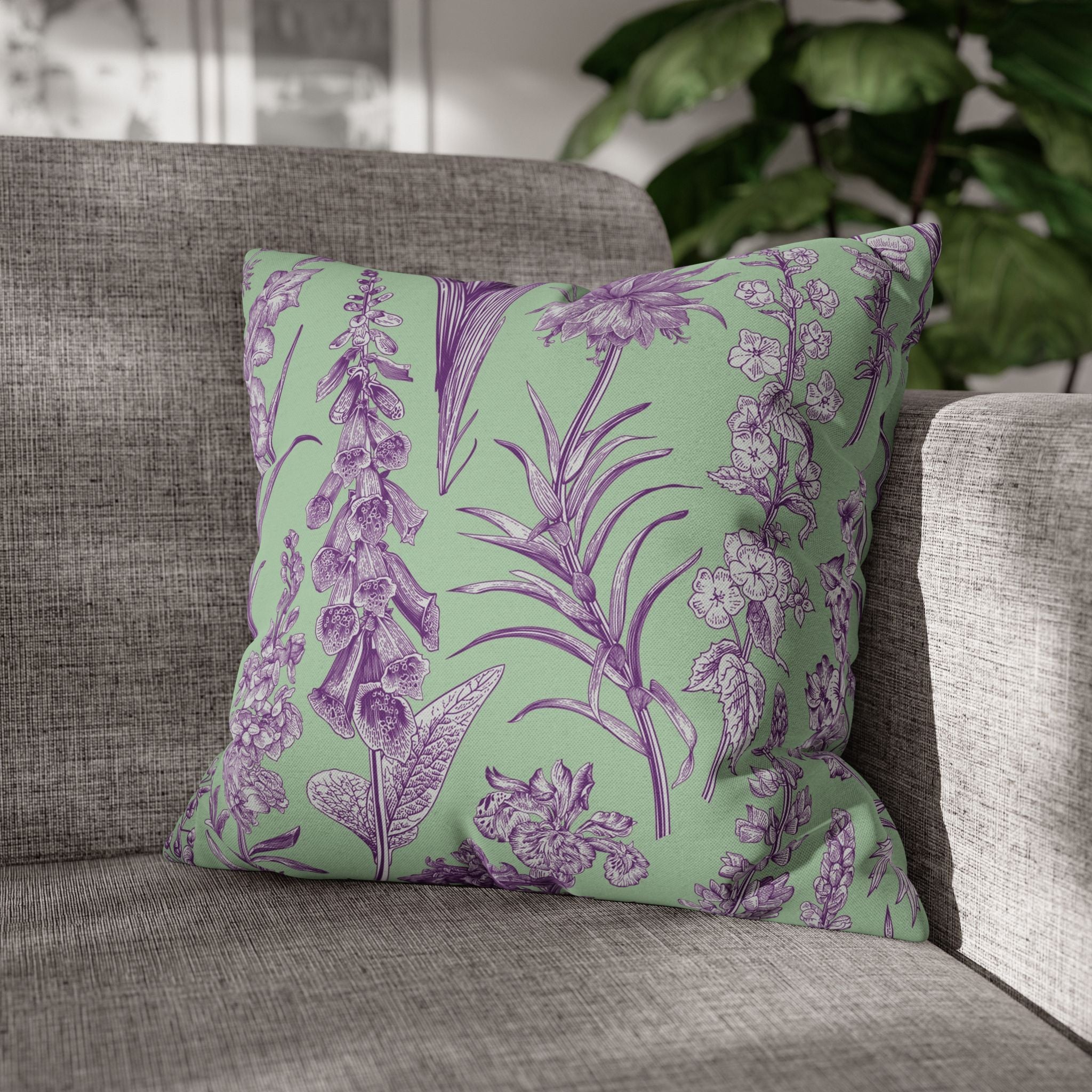 A gray sofa with a green throw pillow featuring a floral pattern in shades of purple and white.