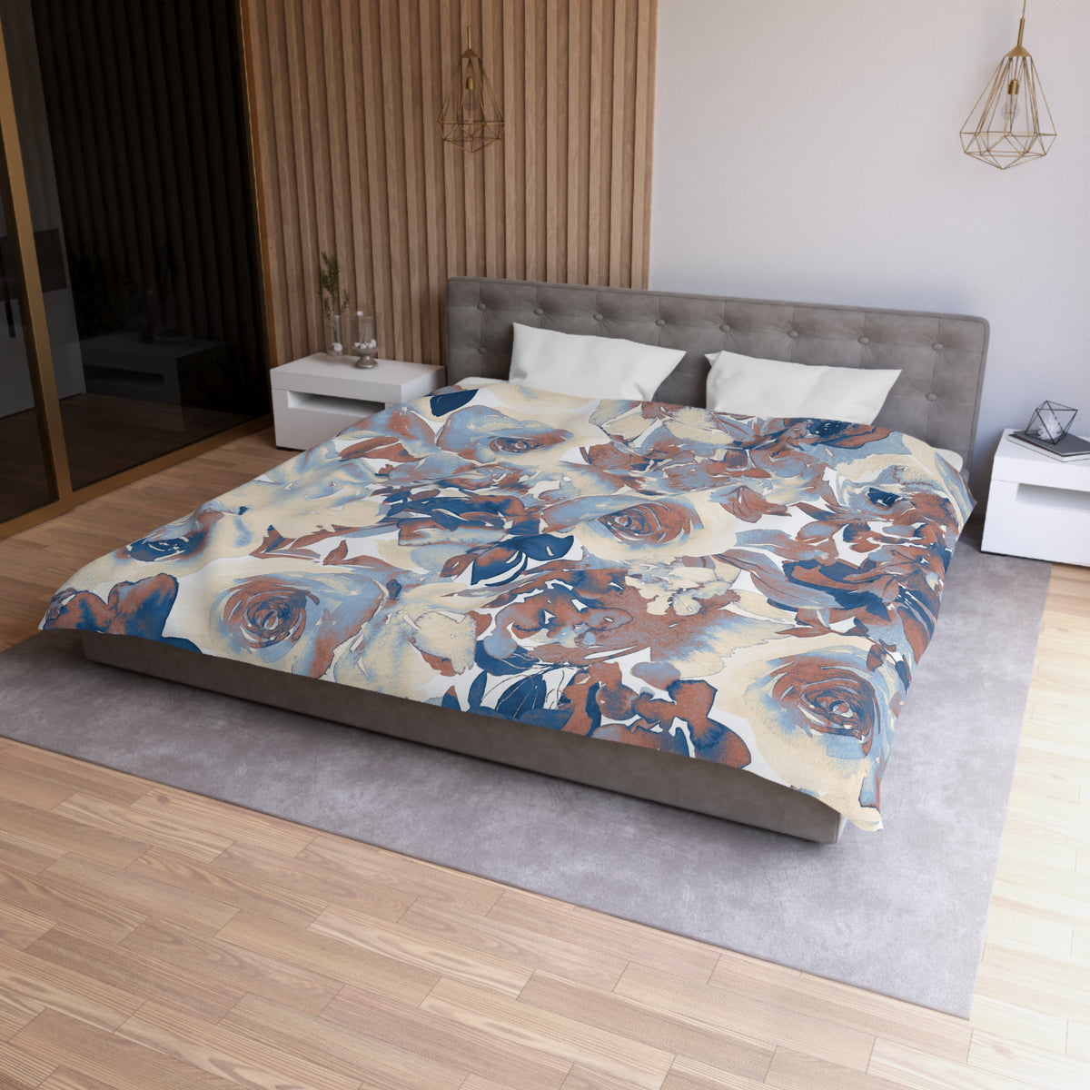 a modern bedroom with a large bed covered in a floral print comforter. The bed is positioned against a wall with a wooden panel. The room has a minimalist design, with a gray headboard and white nightstands. There is a pendant light hanging above the bed, and a vase on one of the nightstands. The overall color scheme of the room is neutral, with pops of blue and brown accents.
