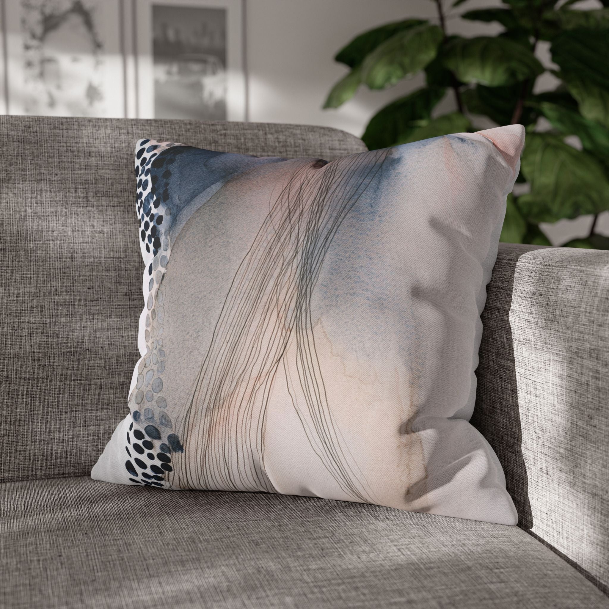 A gray couch with a decorative throw pillow featuring abstract watercolor-style lines and dots on a white background.