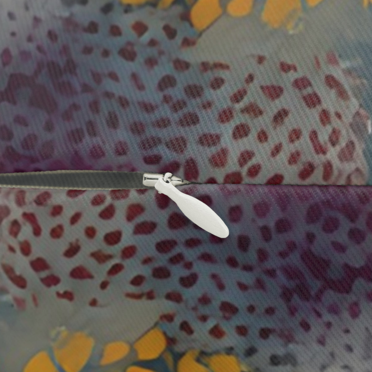 a close-up view of a zipper with a white plastic handle, set against a colorful, abstract pattern with various shades of purple, orange, and yellow.