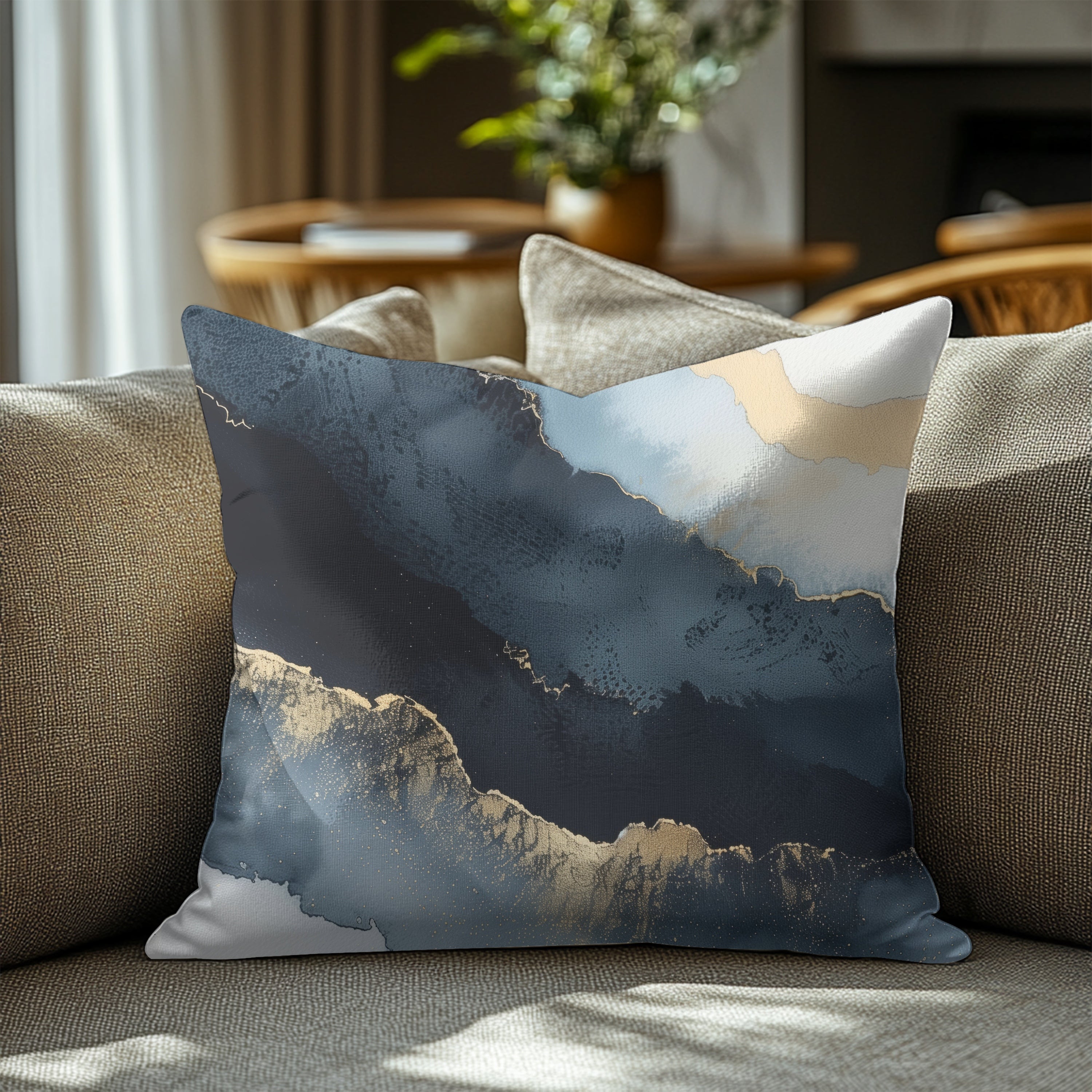 a decorative throw pillow with a striking abstract design, including shades of blue, gray, and gold, placed on a couch in a living room setting.