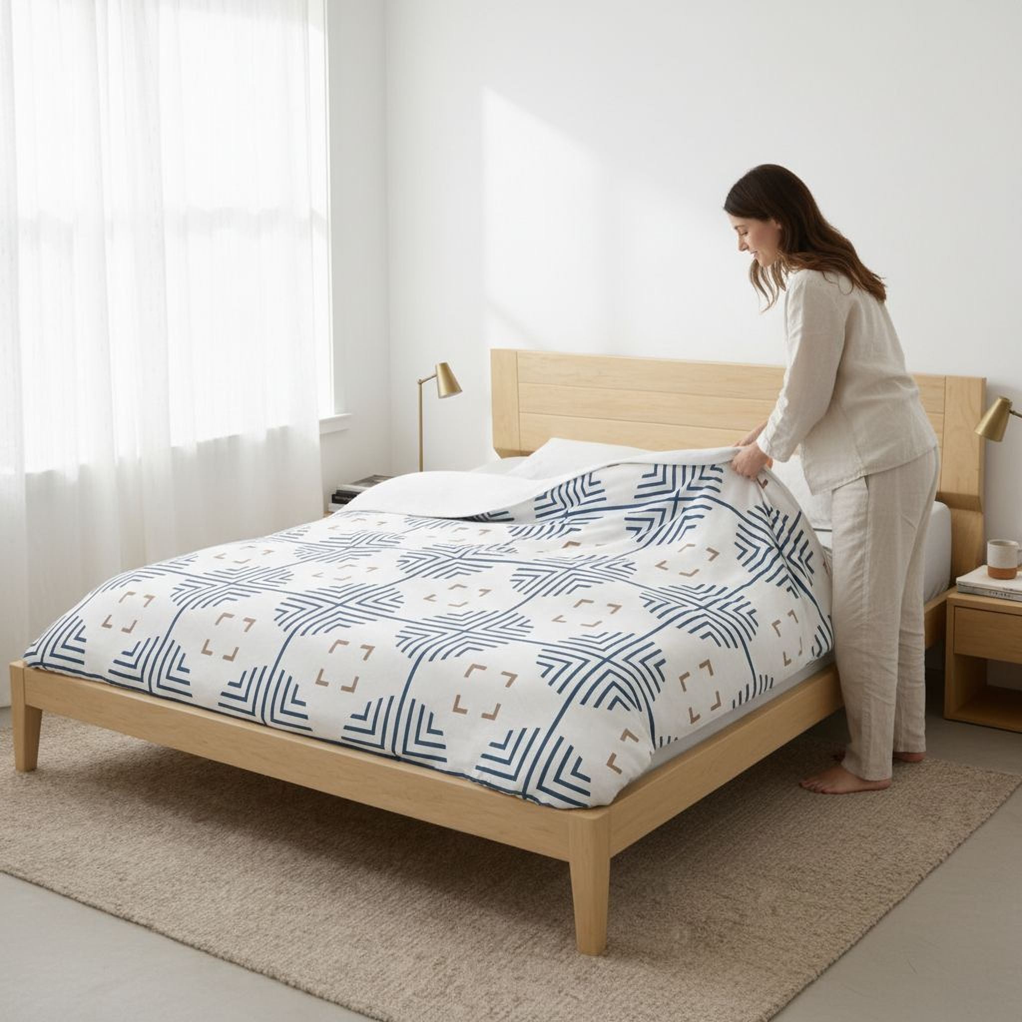 A woman is making the bed in a bedroom with a white and blue patterned comforter.