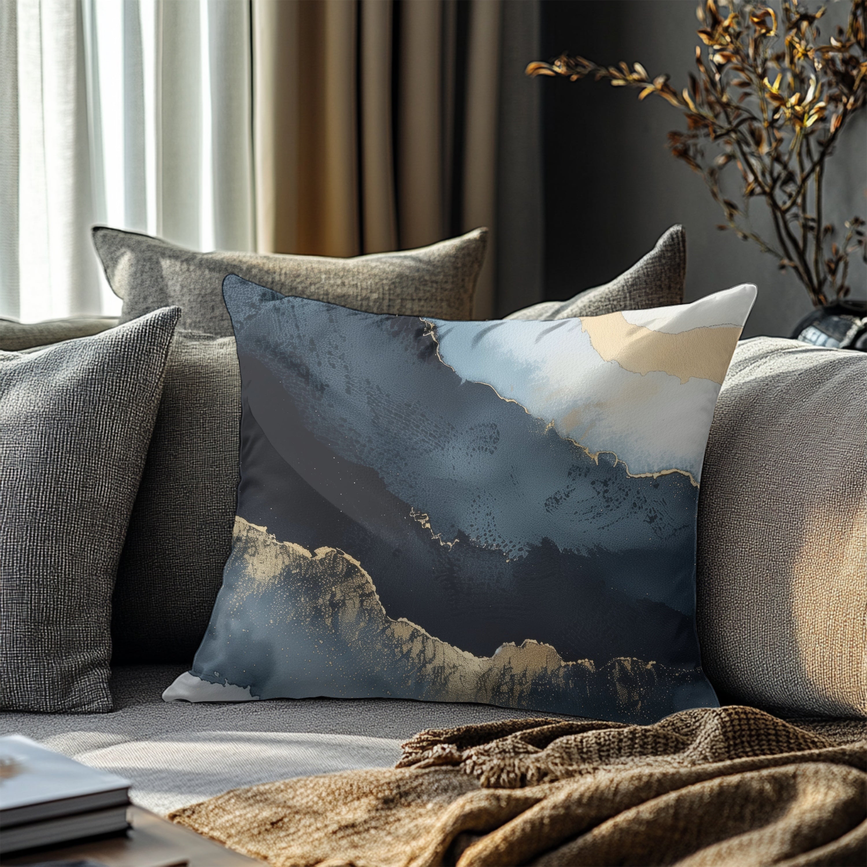 a cozy living room with a gray sofa adorned with a blue and white abstract pillow. The pillow is placed on the sofa, which is covered with a brown blanket. In the background, there is a window with curtains, and a plant can be seen on the windowsill.