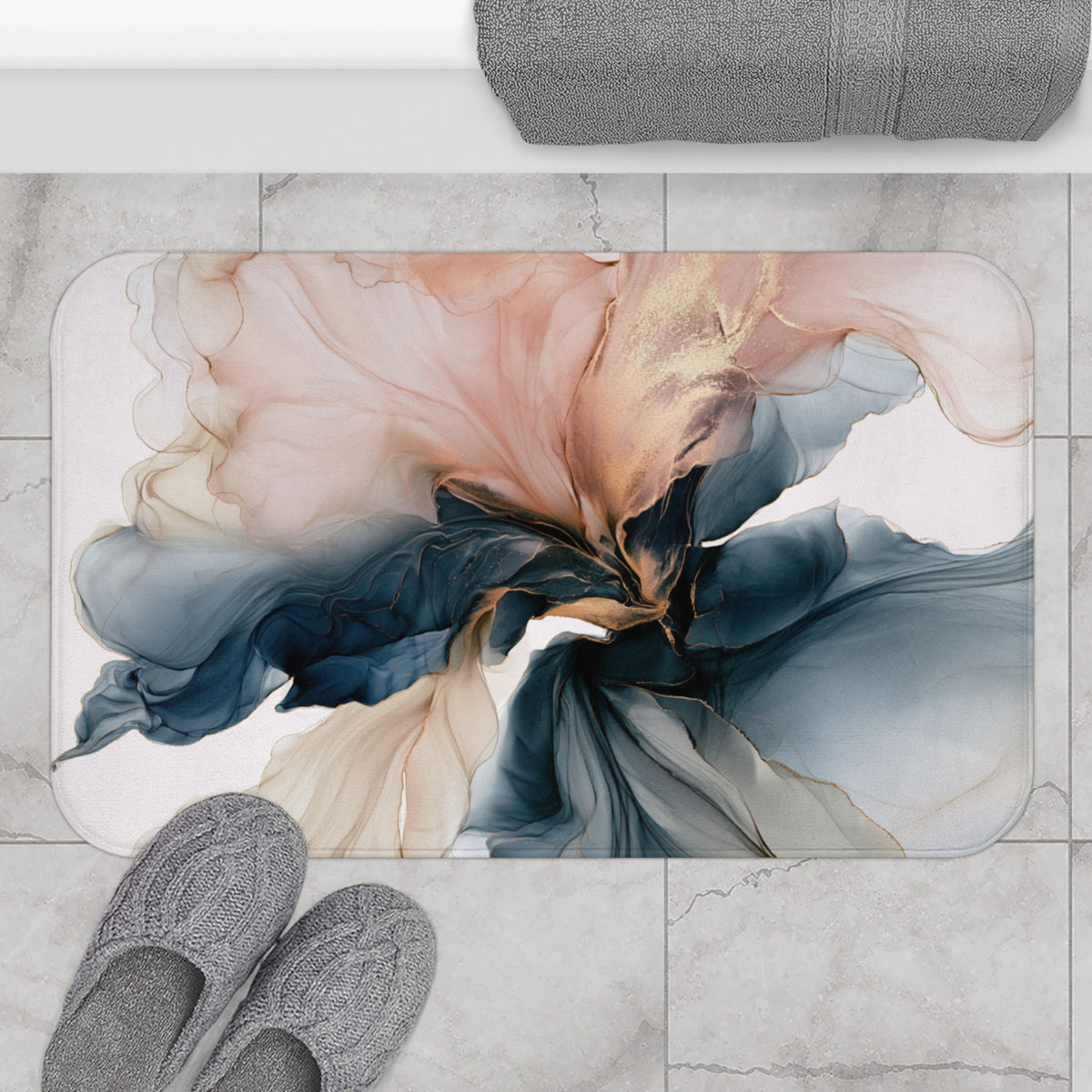 a bathroom mat with a colorful abstract floral design, placed on a tiled floor. Next to the mat, there are a pair of gray slippers and a rolled-up gray towel.