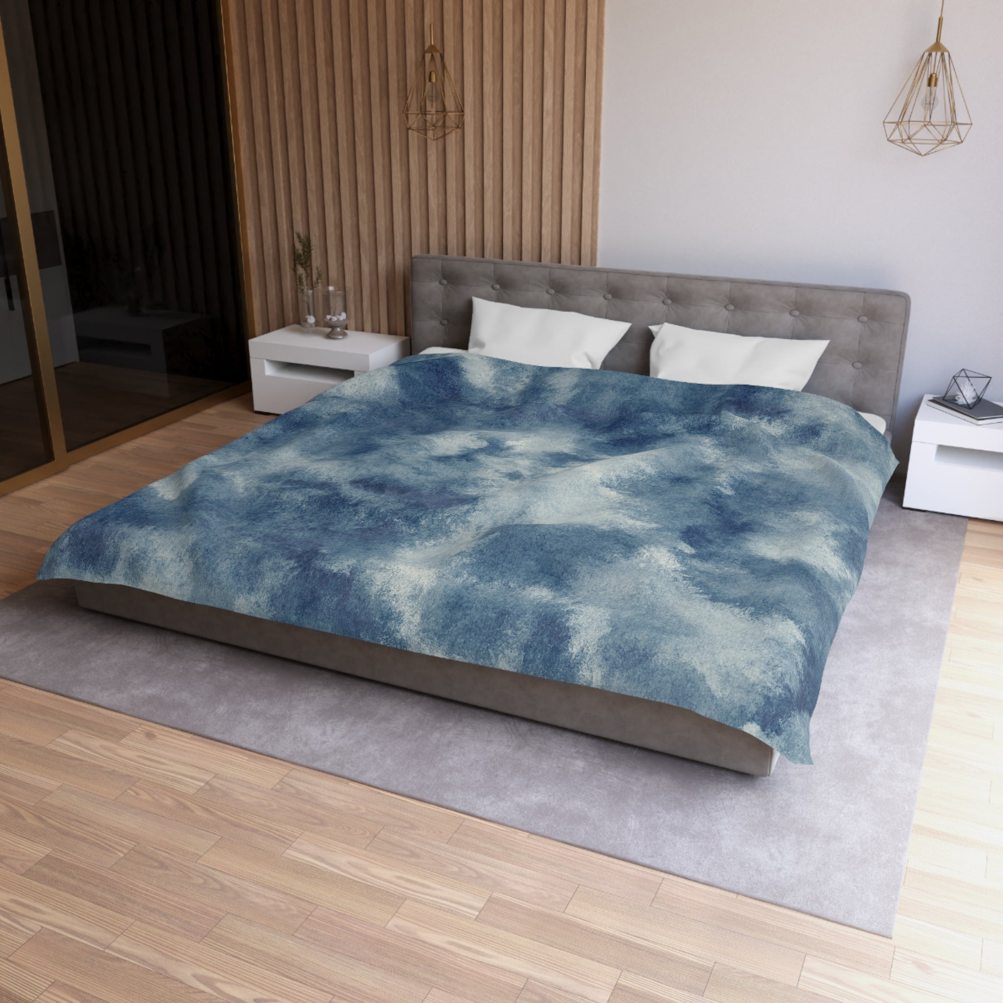 a modern bedroom with a large bed, a gray headboard, and a blue and white patterned comforter. The room has a wooden floor and white walls, creating a serene and stylish atmosphere.