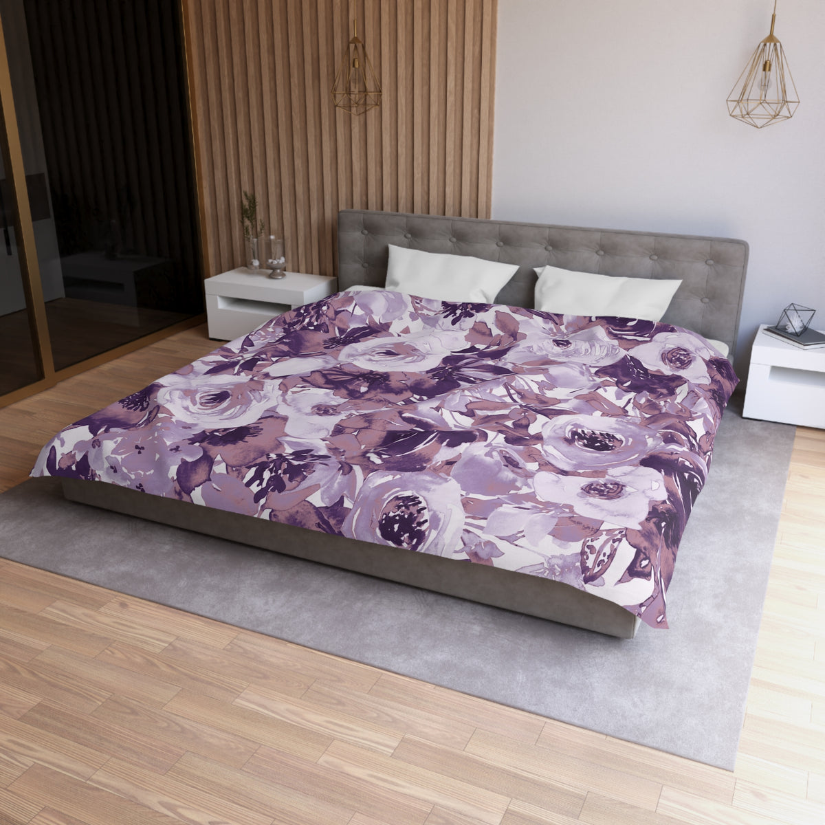 a modern bedroom with a large bed covered in a purple and white floral comforter. The bed is positioned against a wall with a wooden panel. The room also features a nightstand, a pendant light, and a rug on the floor.