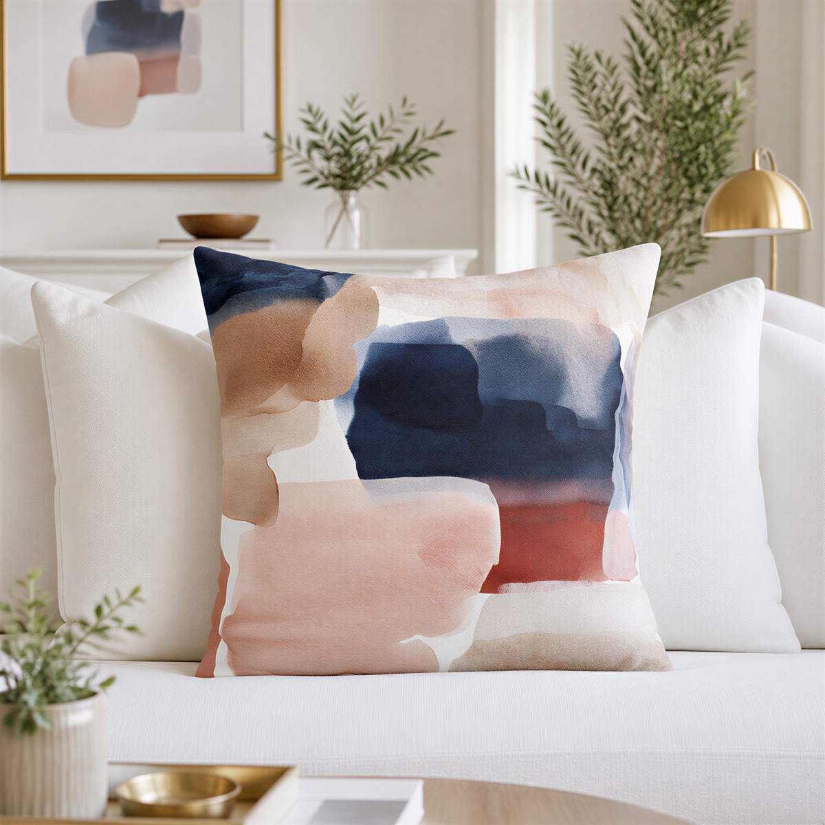 a living room with a white sofa and a decorative throw pillow with an abstract watercolor painting design in shades of blue, pink, and white. The room also includes a potted plant, a vase, and a lamp, creating a cozy and inviting atmosphere.