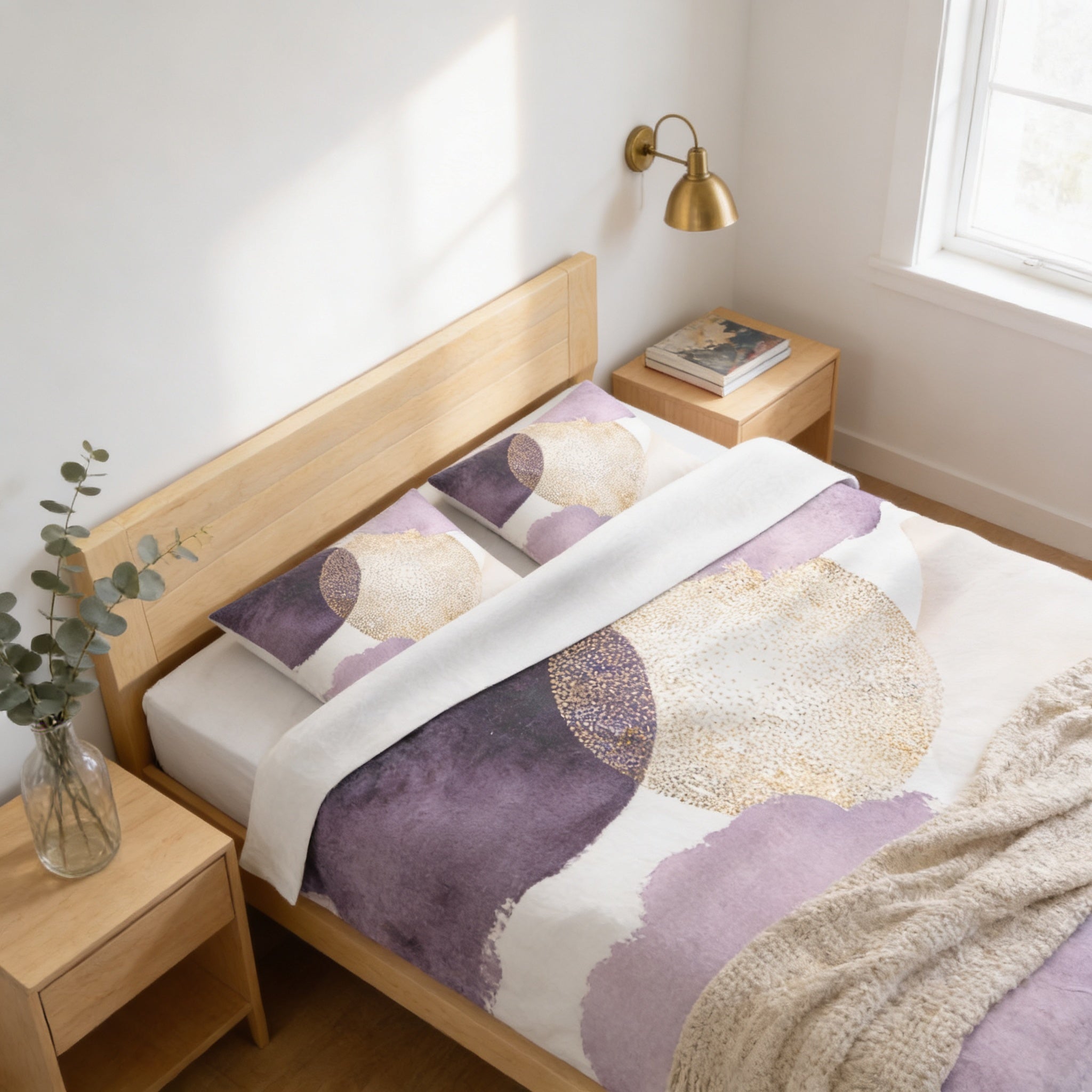 a bedroom with a bed, nightstand, and a window. The bed has a purple and white patterned comforter and matching pillows. The nightstand has a lamp and a book on it. The window allows natural light to enter the room.