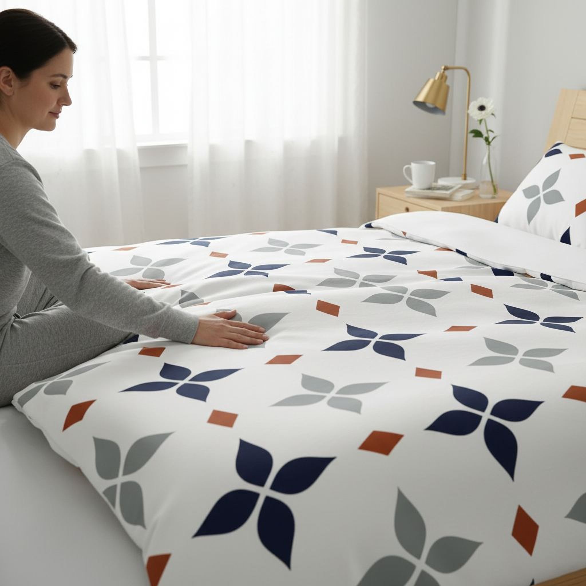 A woman is sitting on a bed, touching the patterned comforter.