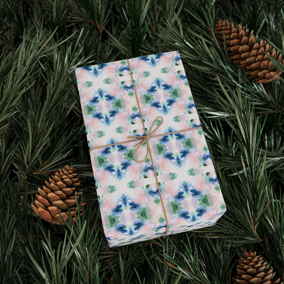 Gift wrapped in blush, blue and green mirrored watercolor wrapping paper on pine branches with pinecones