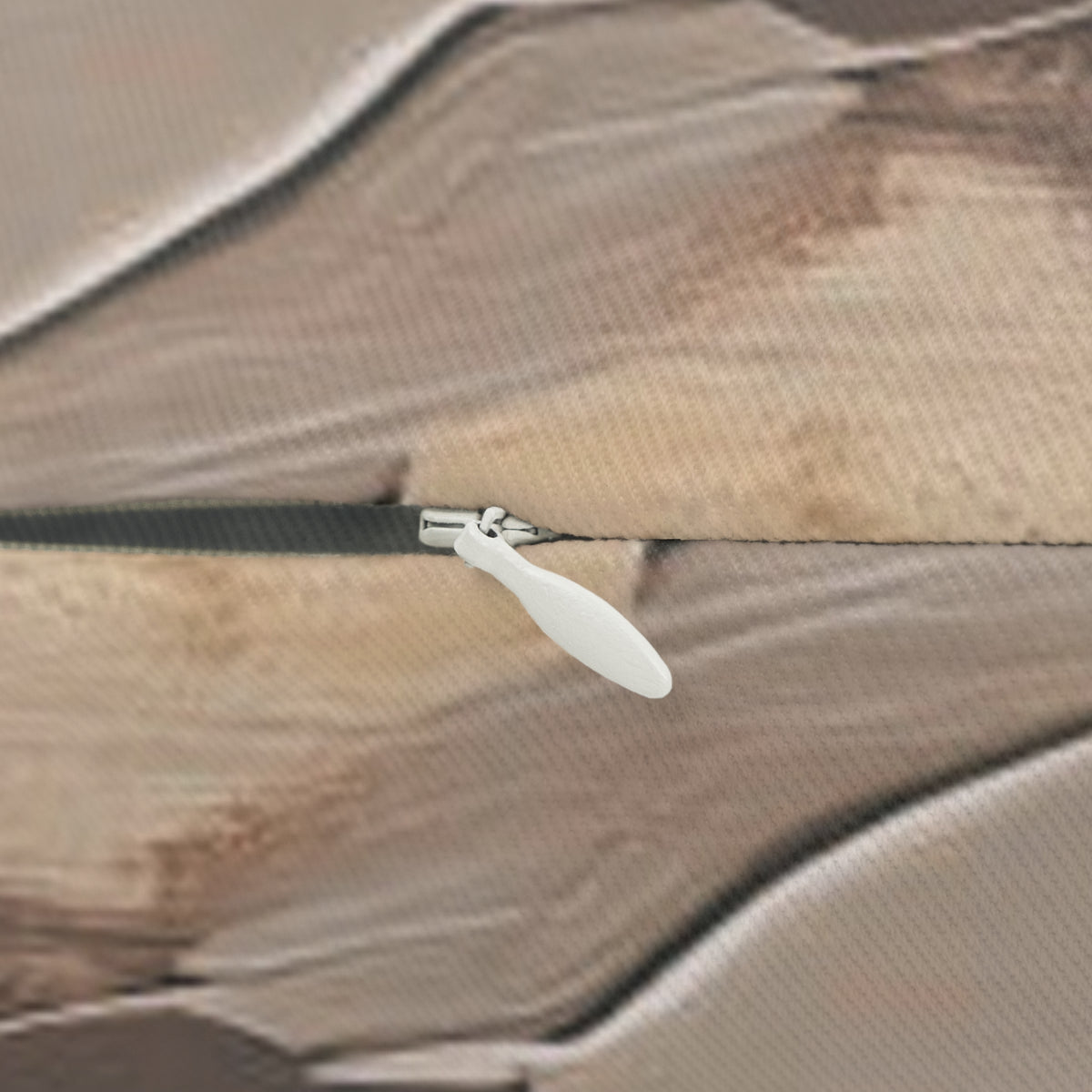 A close-up view of a white zipper pull on a brown fabric surface.