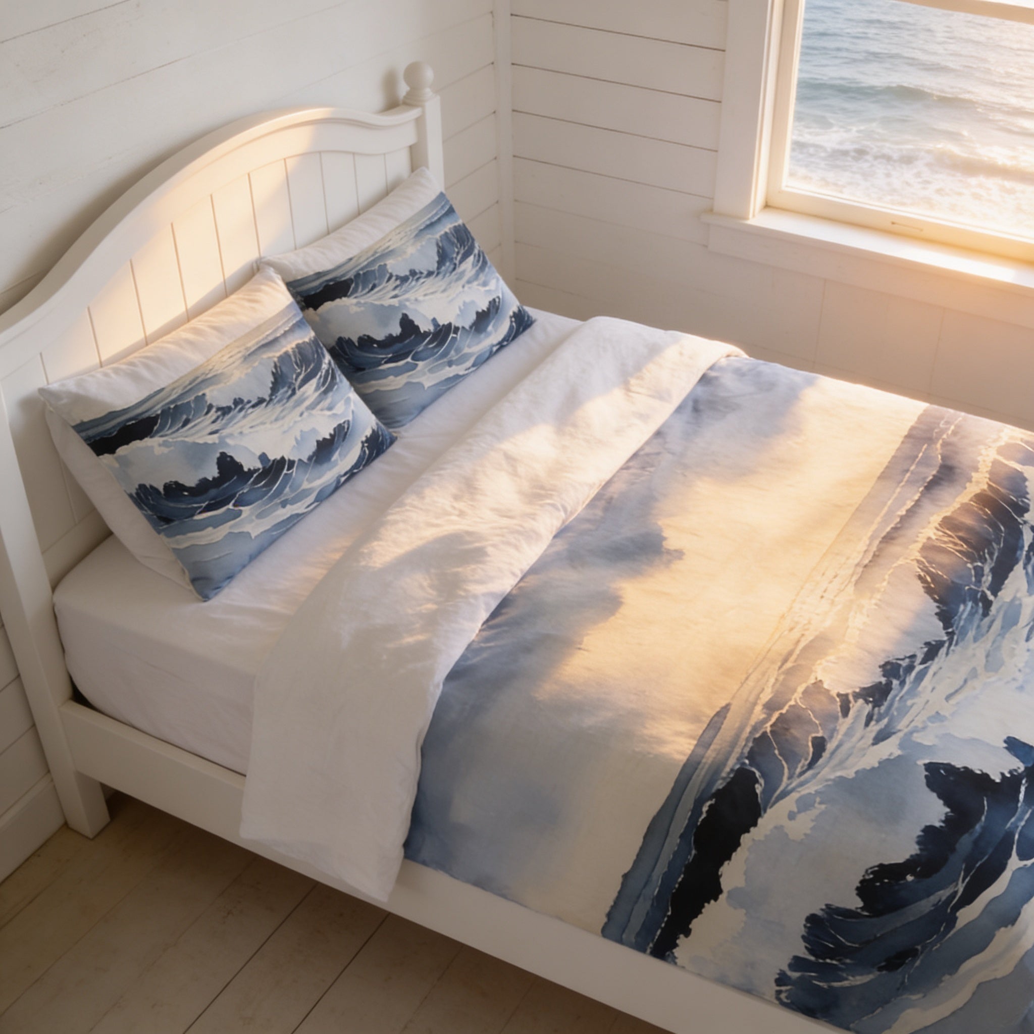 a cozy bedroom with a white wooden bed frame, a white headboard, and a blue and white patterned comforter. The bed is positioned near a window that offers a view of the ocean, creating a serene and peaceful atmosphere.