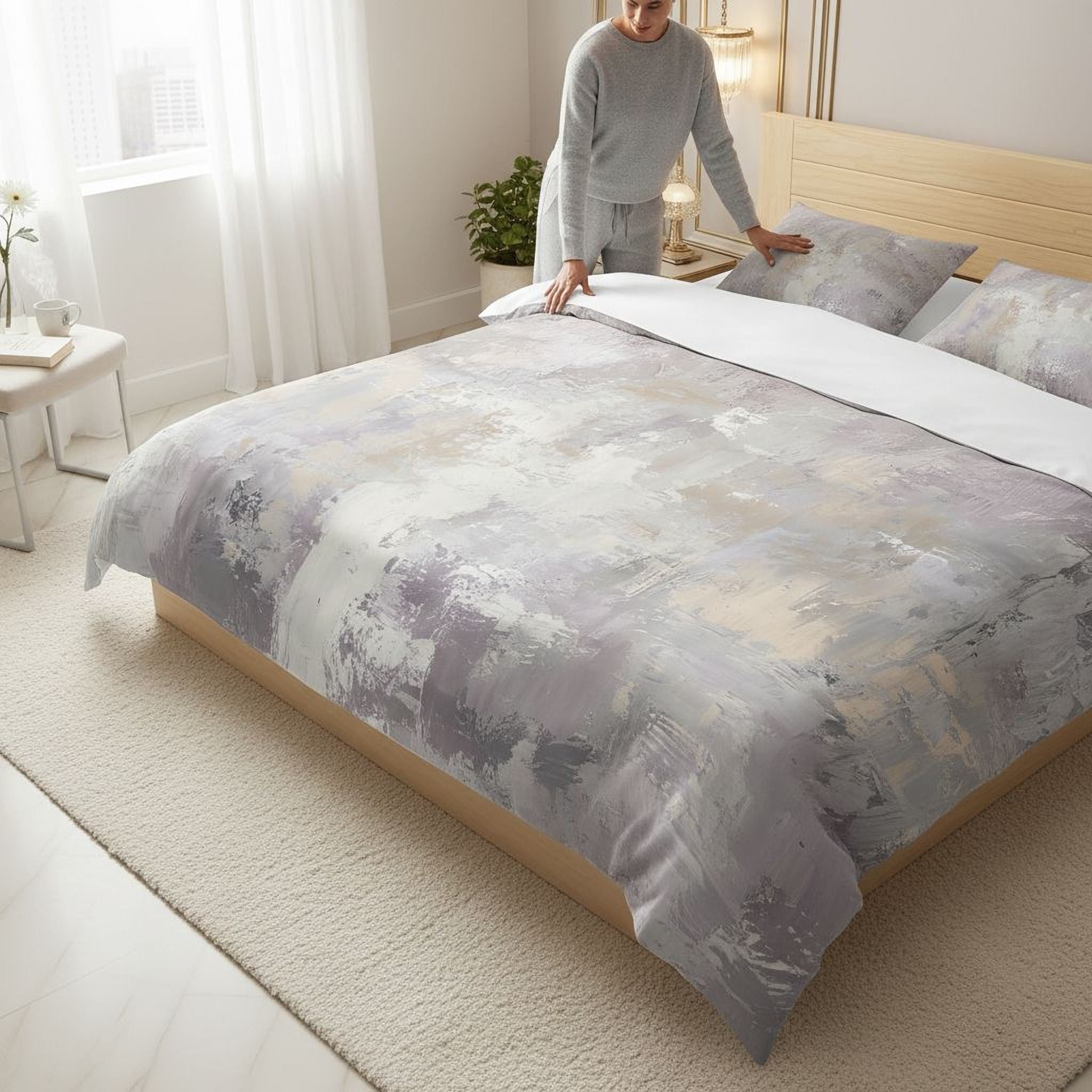 A person is arranging a bed with a gray and white patterned comforter and pillows in a bedroom.