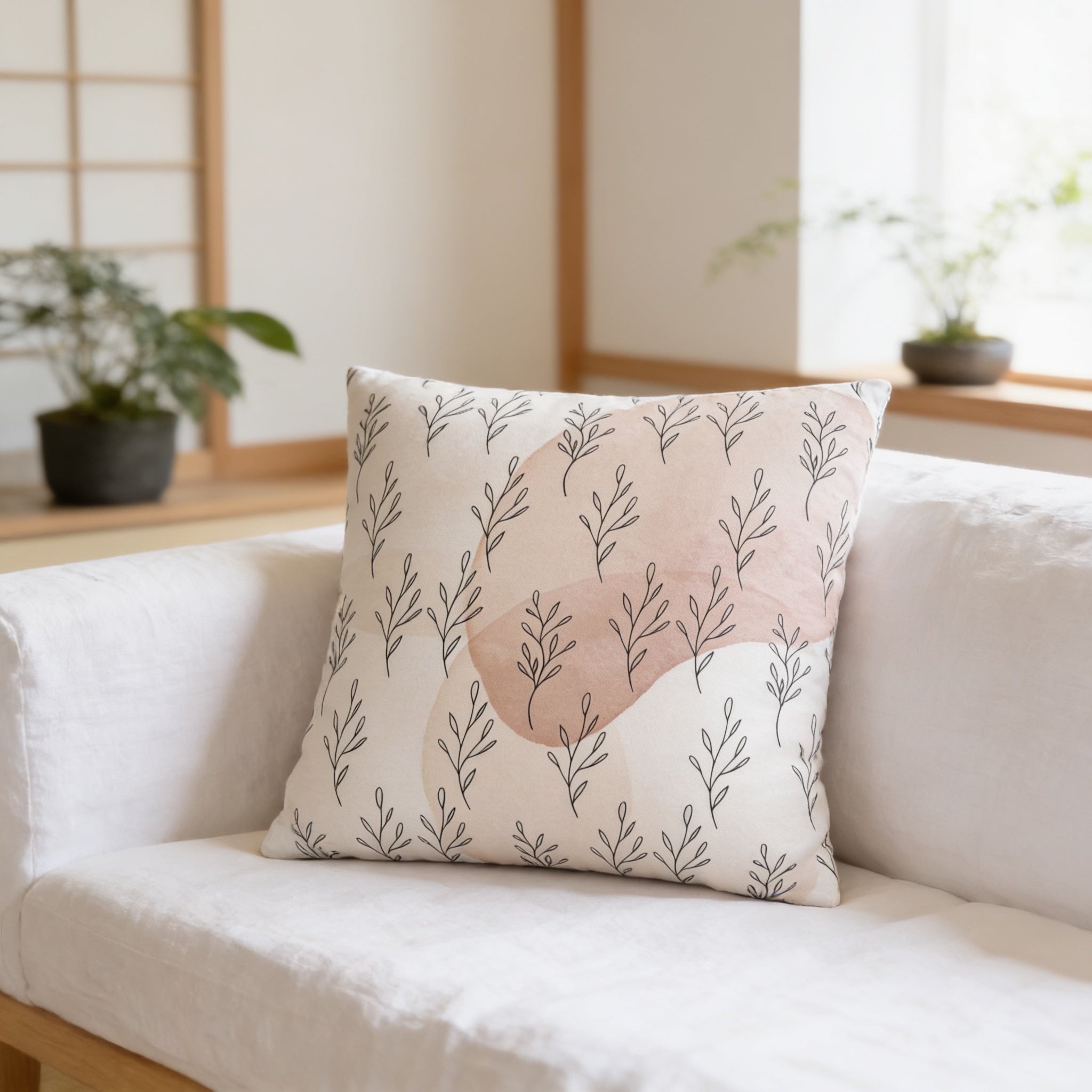 a white sofa with a decorative throw pillow featuring a repeating pattern of leaves and branches in shades of pink and white.