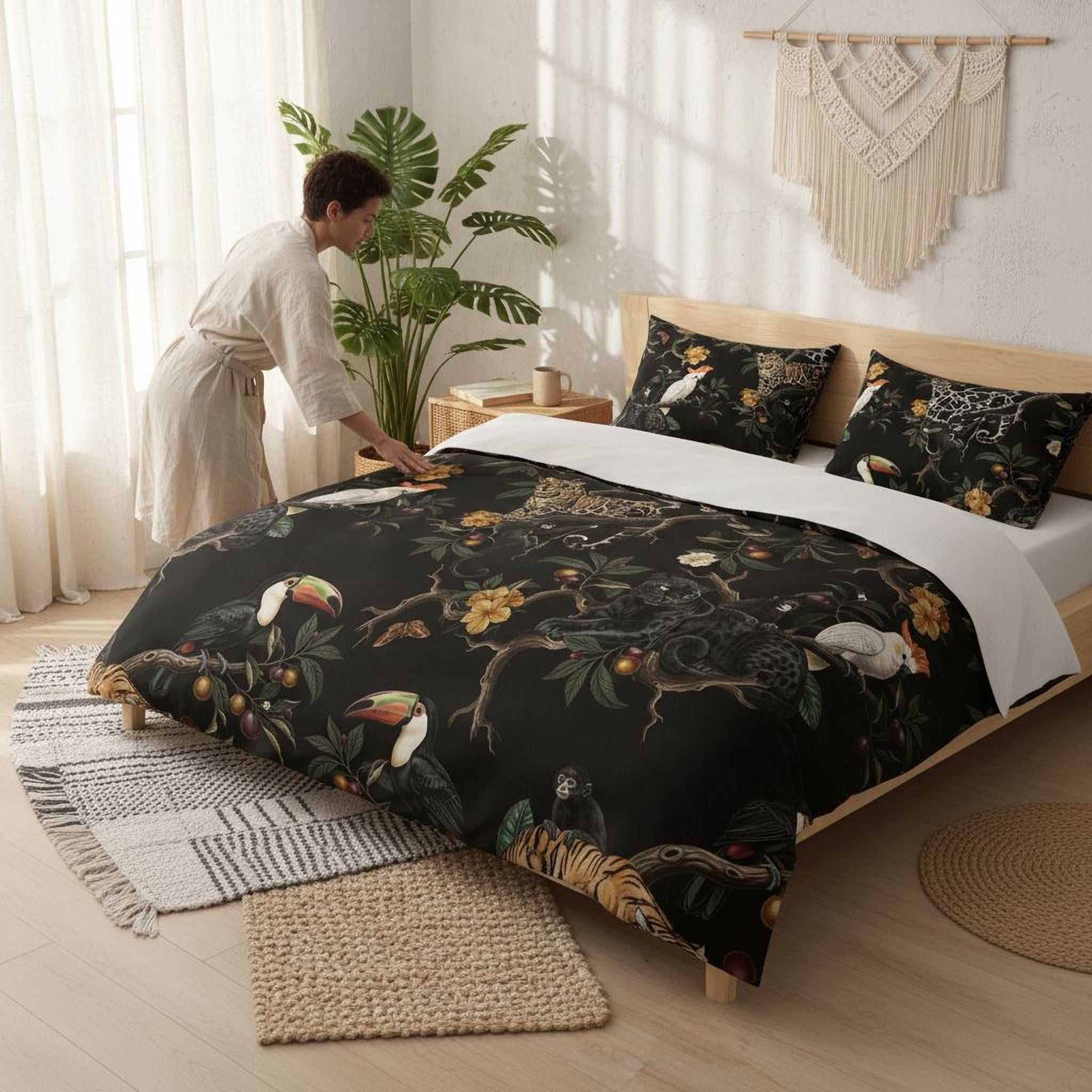 A person is arranging a bed with a black and gold patterned comforter featuring tropical birds and animals, including a parrot and a tiger.