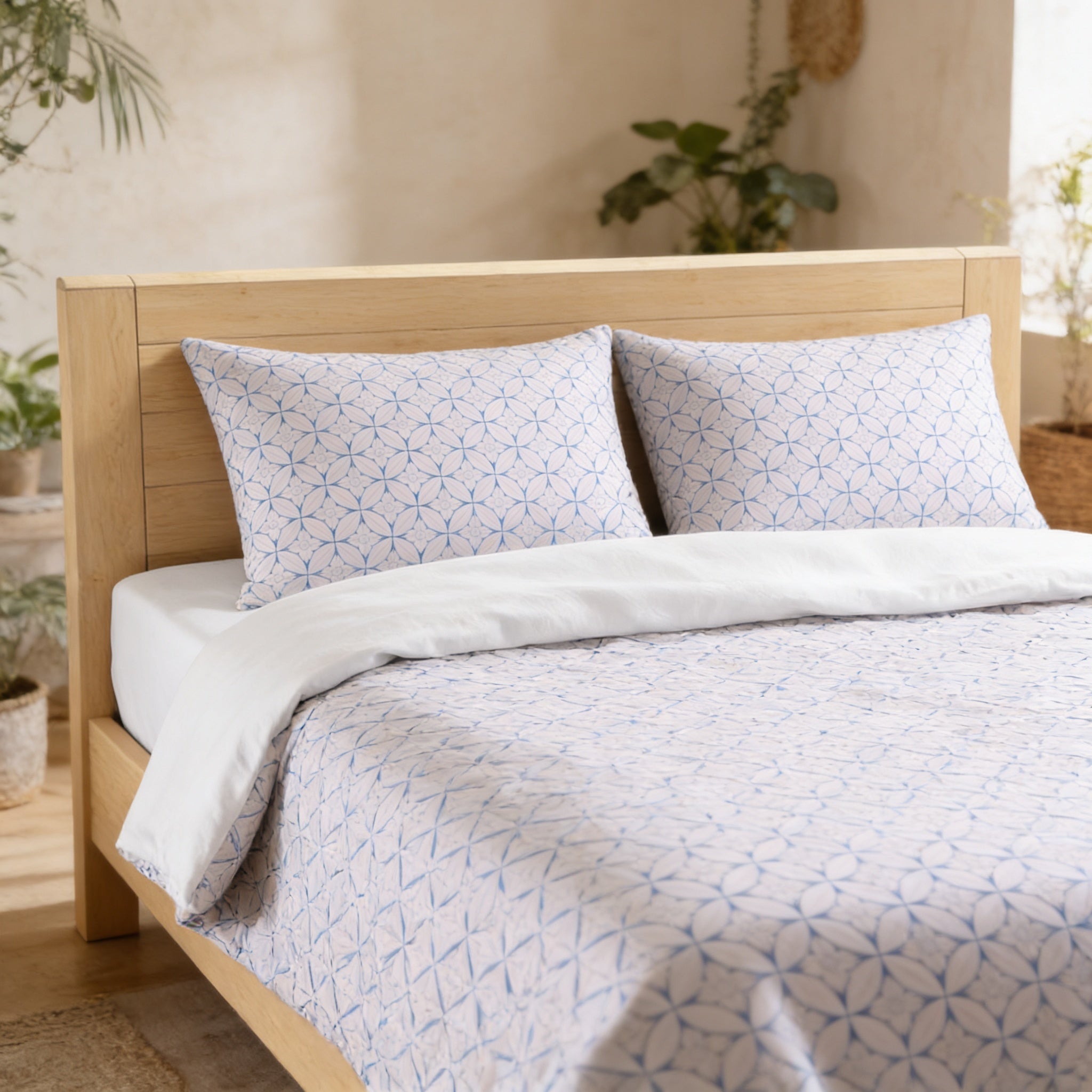 a neatly made bed with a white and blue patterned comforter and pillows, set against a backdrop of a wooden headboard and a wall with plants.