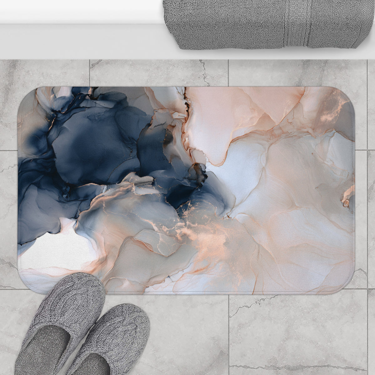 a bathroom rug with a marble-like design in shades of blue, pink, and white. The rug is placed on a tiled floor, and there are gray slippers positioned next to it.
