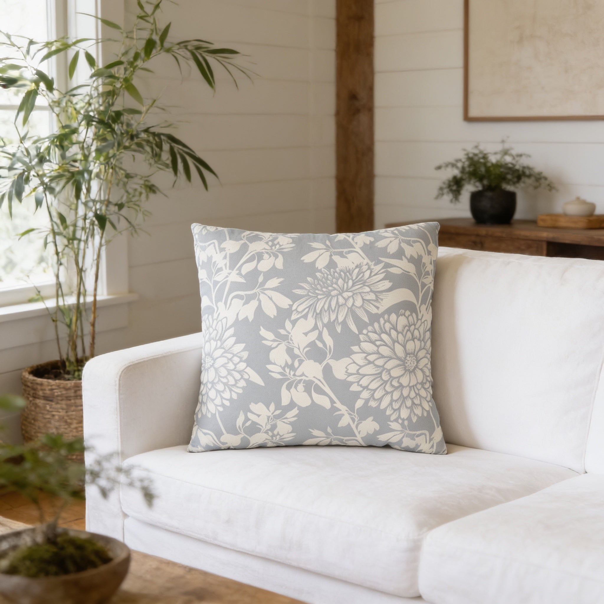 a living room with a white sofa, a gray and white floral throw pillow, and several potted plants.