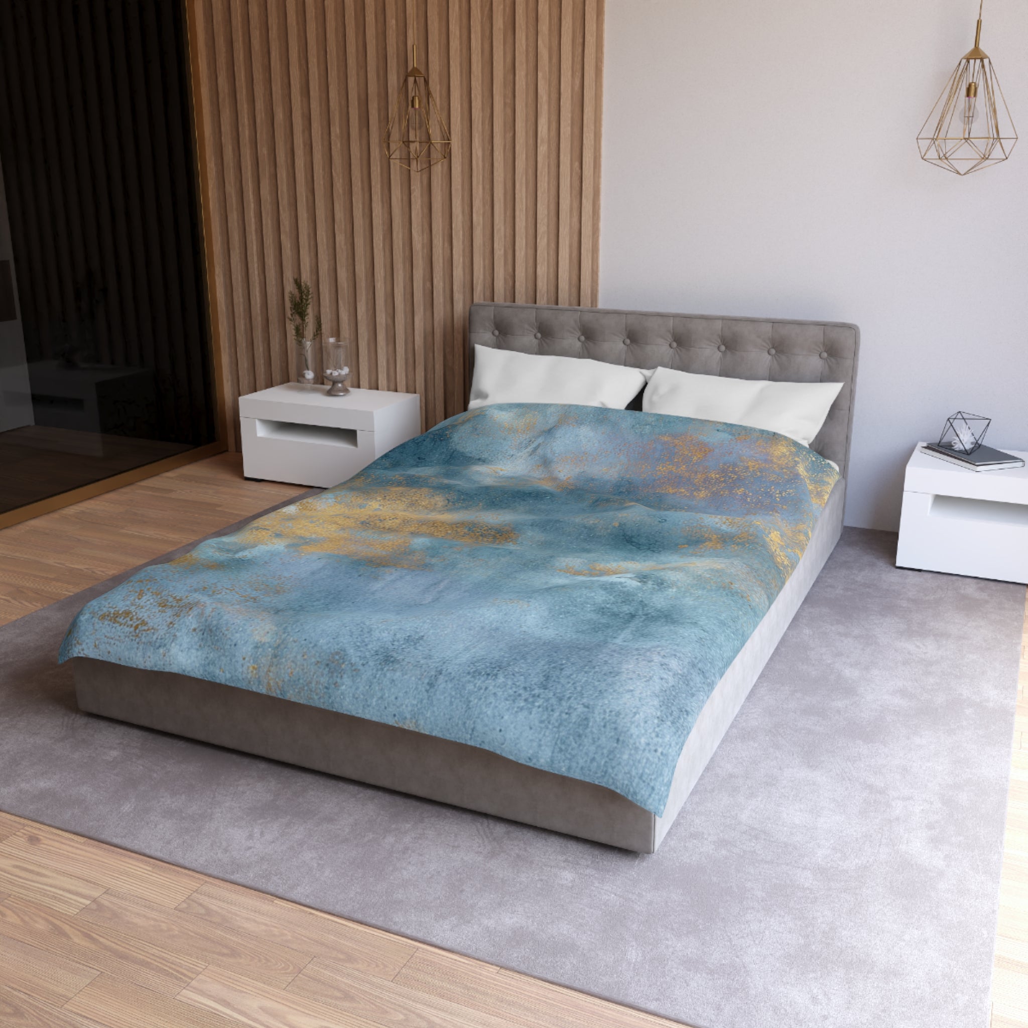 a modern bedroom with a large bed, a gray headboard, and a blue and gold patterned comforter. The room has a neutral color scheme with white walls and a wooden floor. There are two nightstands on either side of the bed, and a pendant light hangs above the bed.