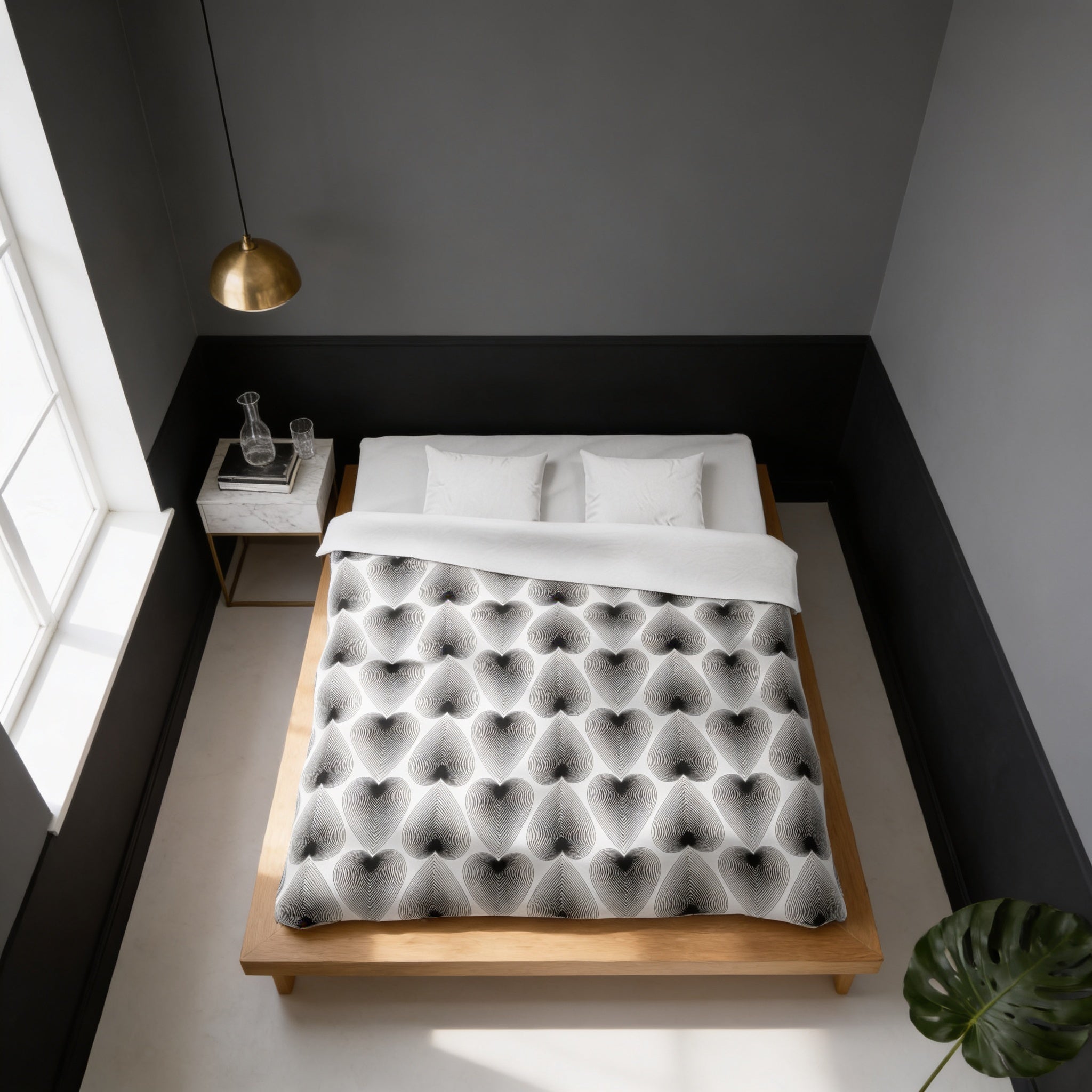 a modern bedroom with a bed, a nightstand, and a pendant light. The bed has a black and white patterned comforter and white pillows. The room has a minimalist and clean design, with gray walls and a wooden floor.