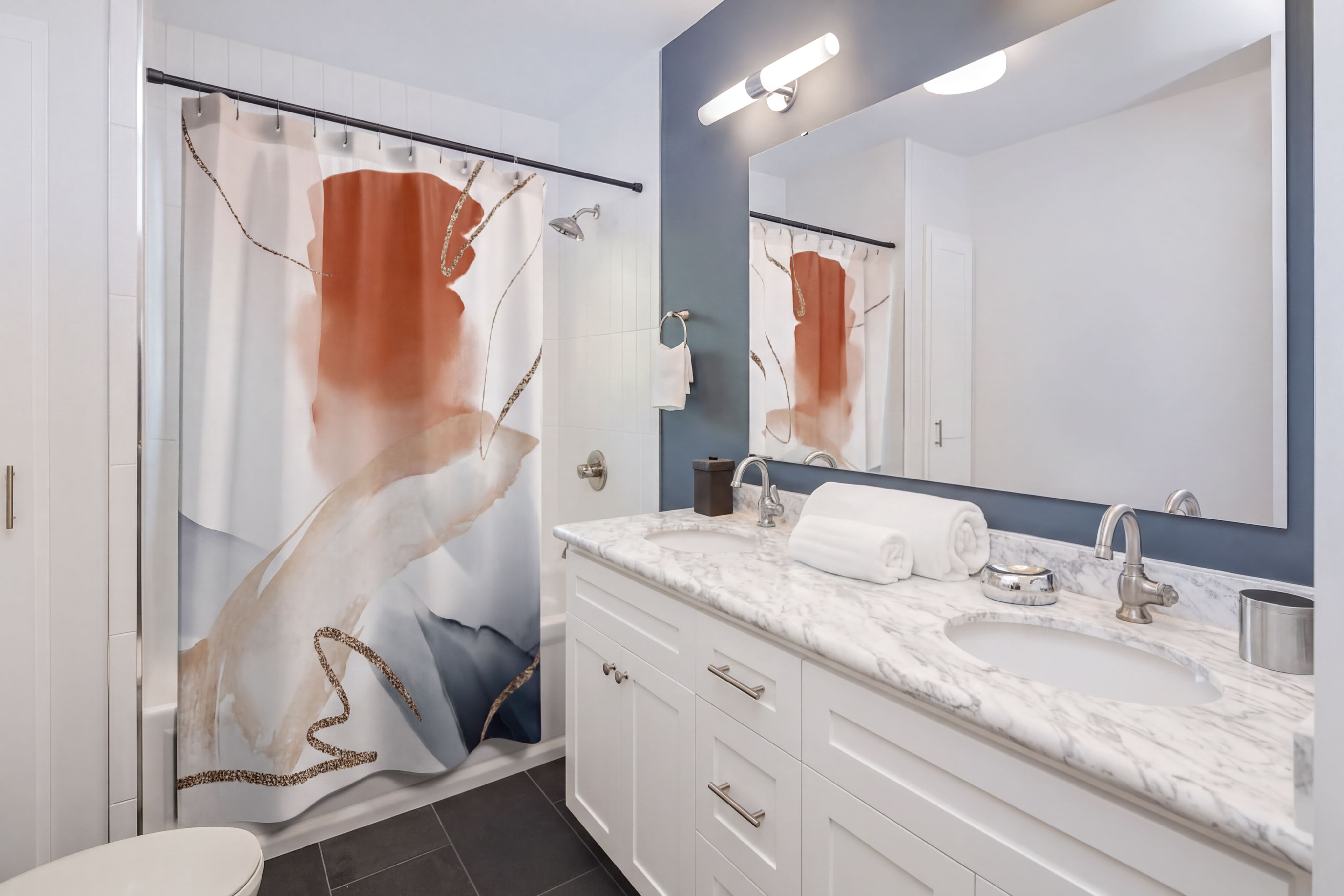 a modern bathroom with a white vanity, marble countertop, and a large mirror. The shower curtain has a colorful abstract design.